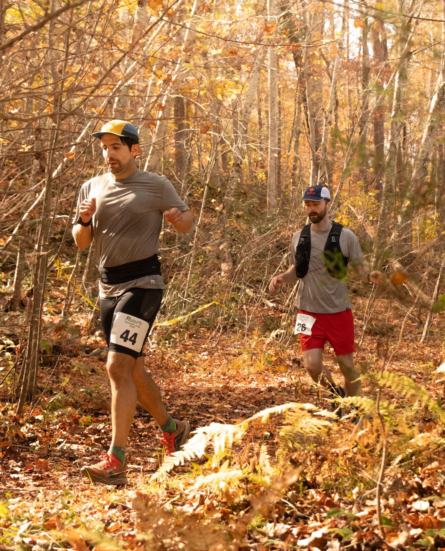 A person performs dynamic stretching exercises in an autumn forest with fallen leaves covering the ground.