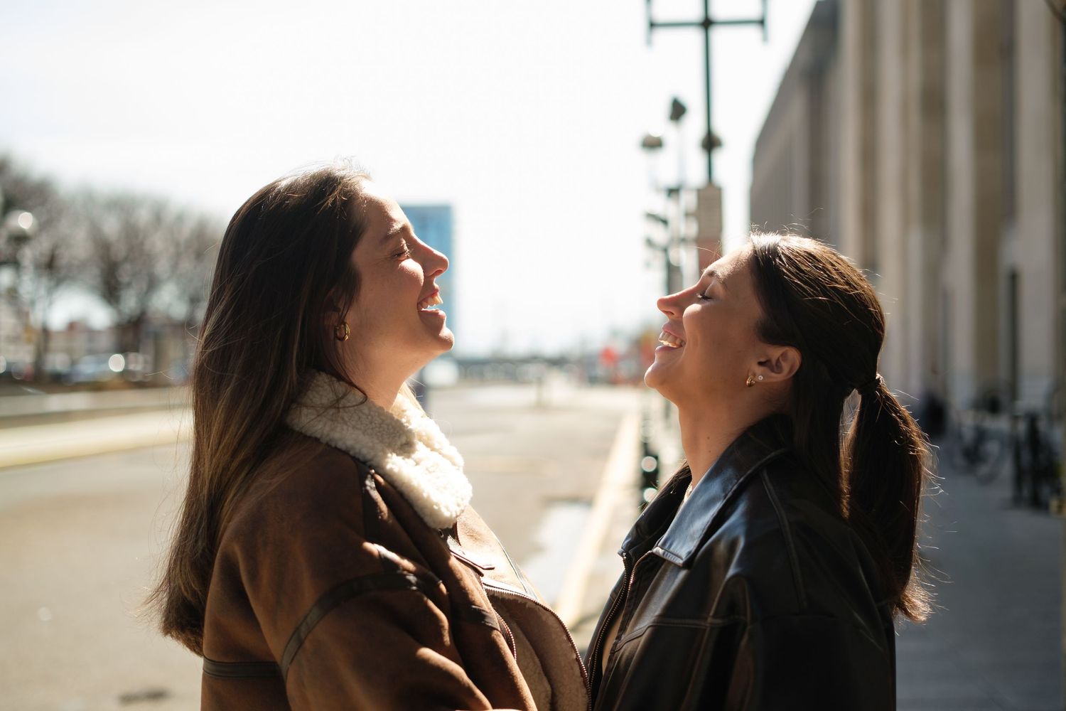 Two people share a joyful laugh while standing outdoors on a sunny day.