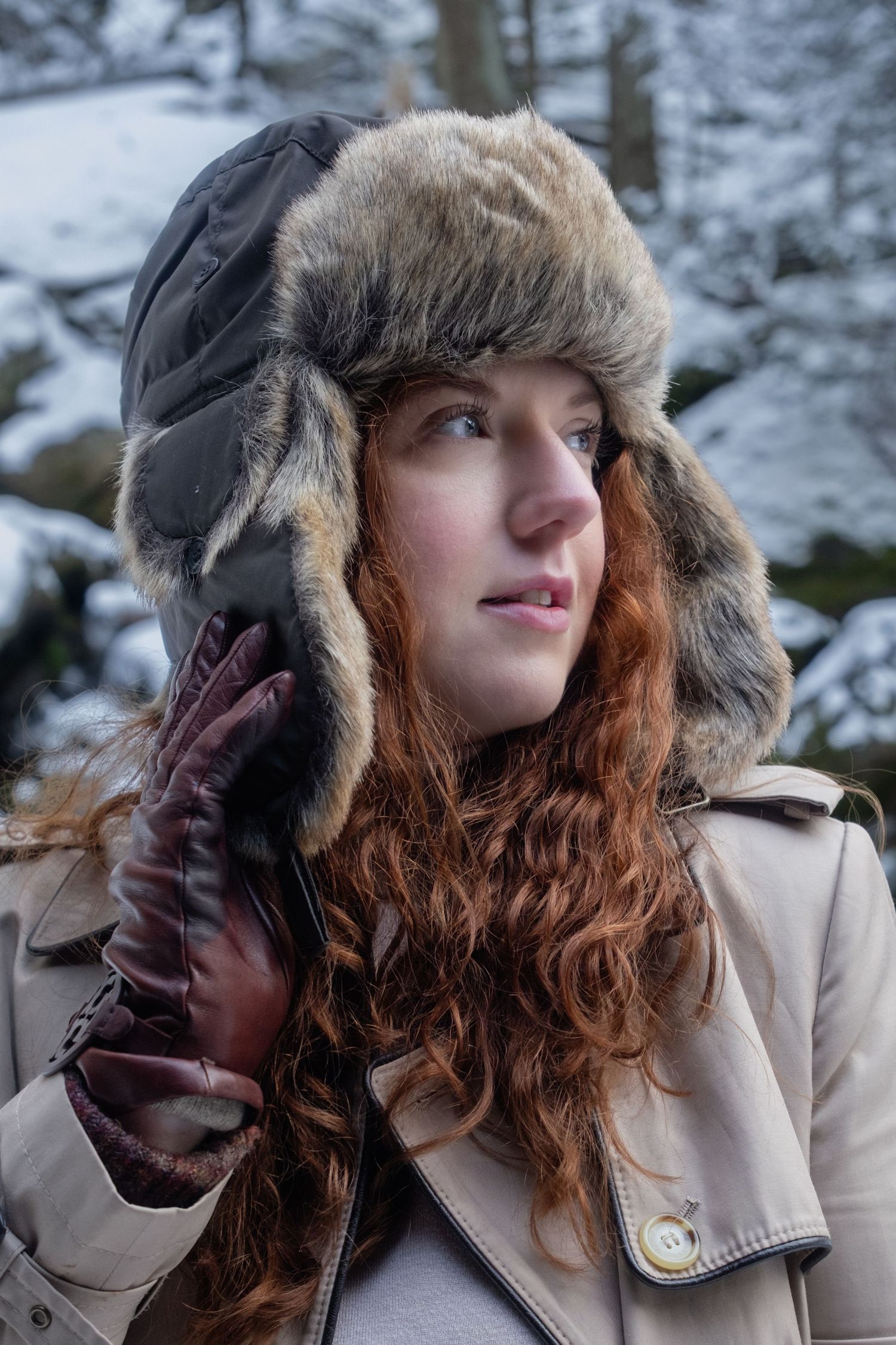 A series of winter portraits showing someone wearing a fur-trimmed hooded coat with flowing red curly hair in snowy scenery.