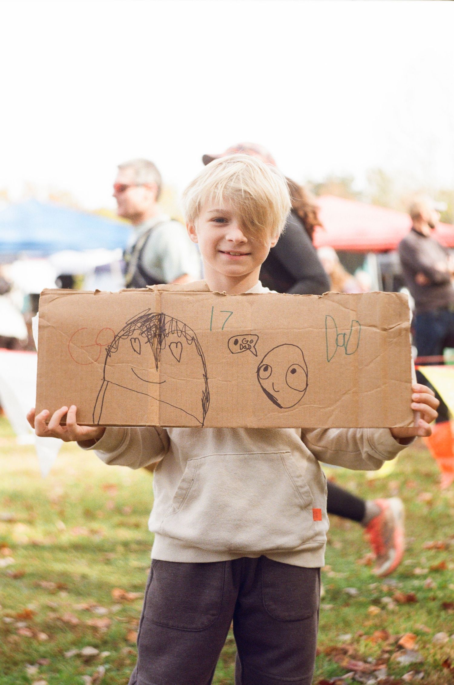 A child holds a long piece of wood with drawings on it while standing in a grassy outdoor area.