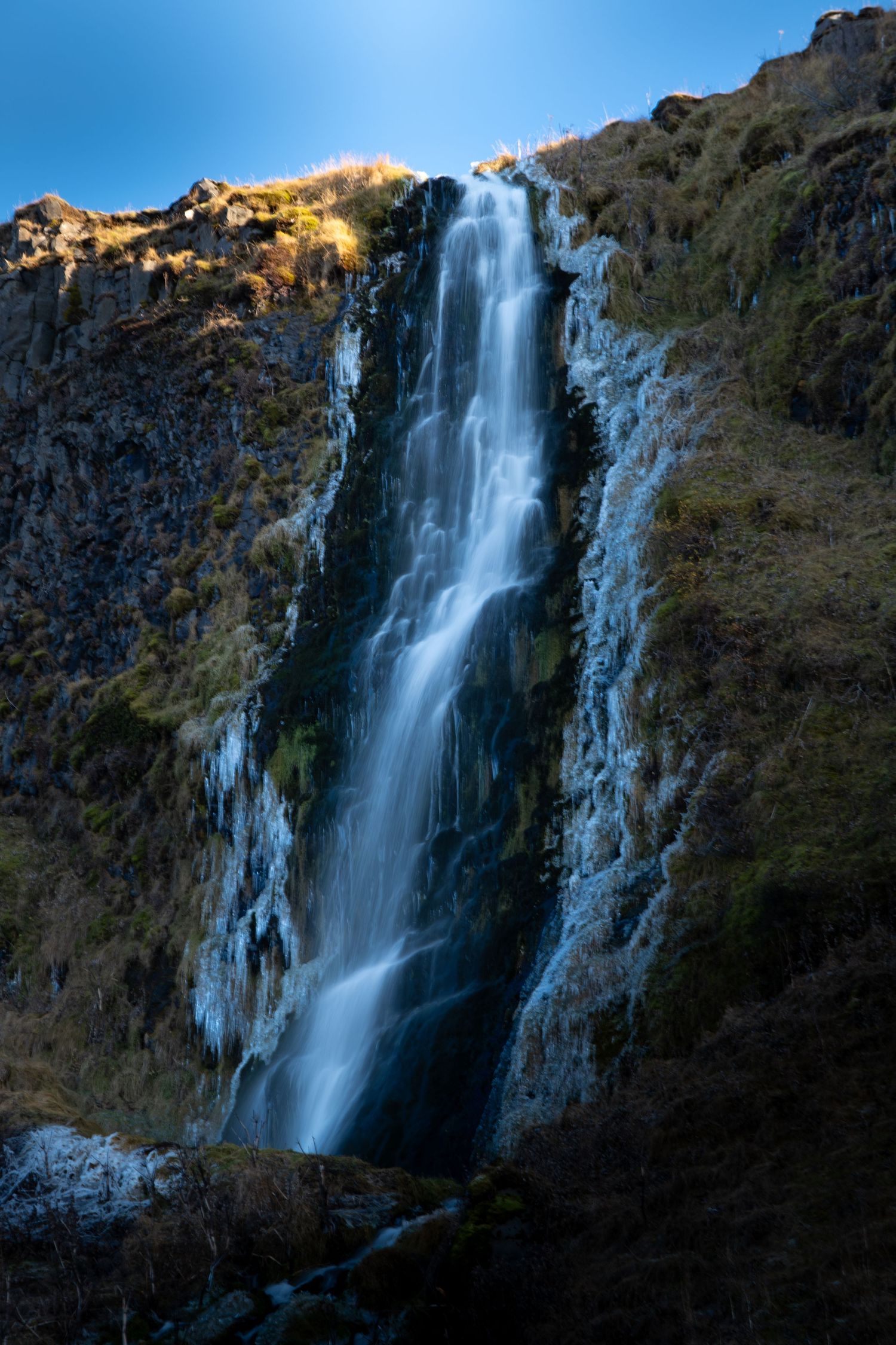 A series of cascading waterfalls flowing down dark rocky cliffs at sunset with golden light illuminating the mountainside.