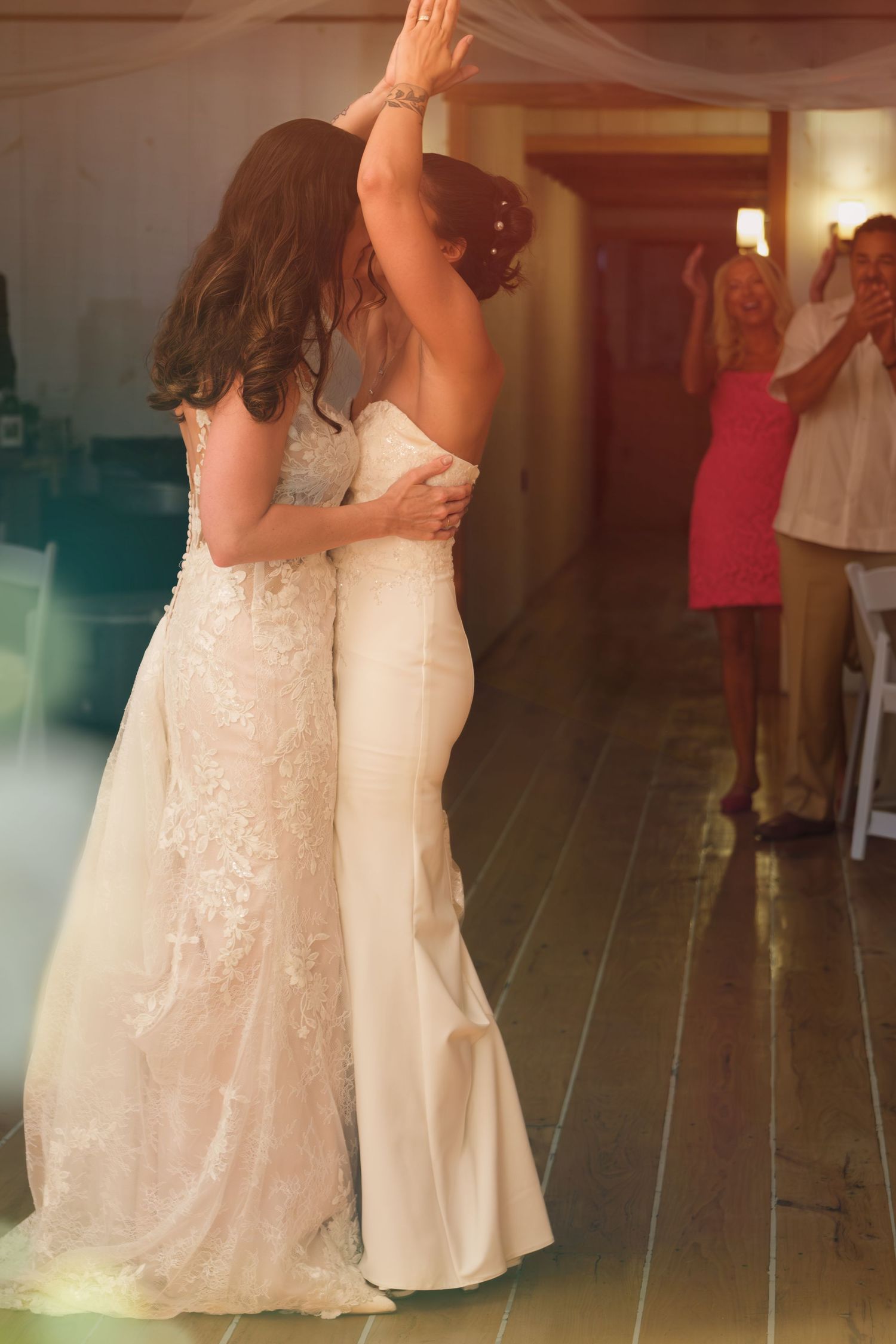 Two brides share a first dance in white wedding gowns while guests celebrate in the background.