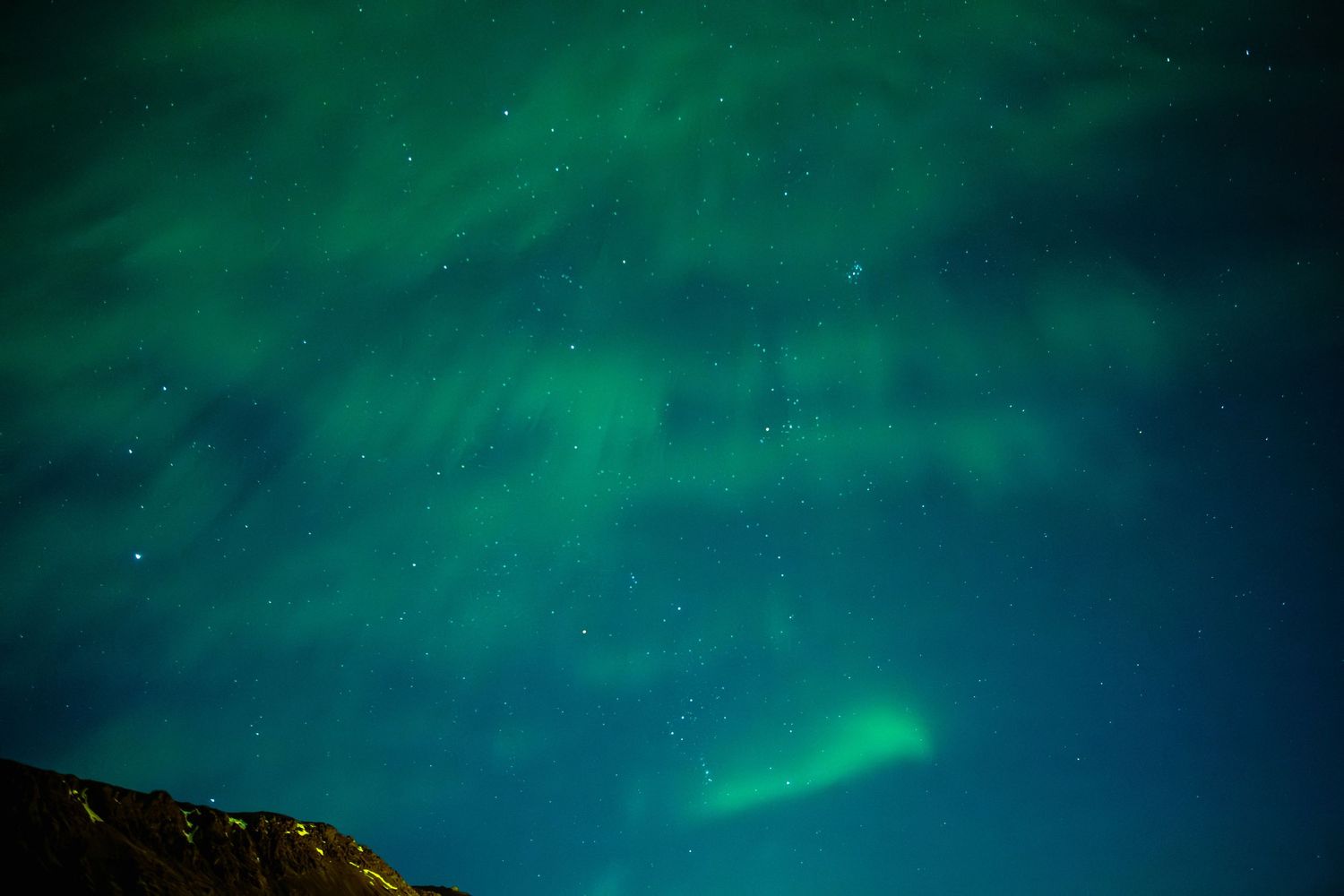 Vibrant green northern lights dance across a dark night sky above a silhouetted mountain landscape.