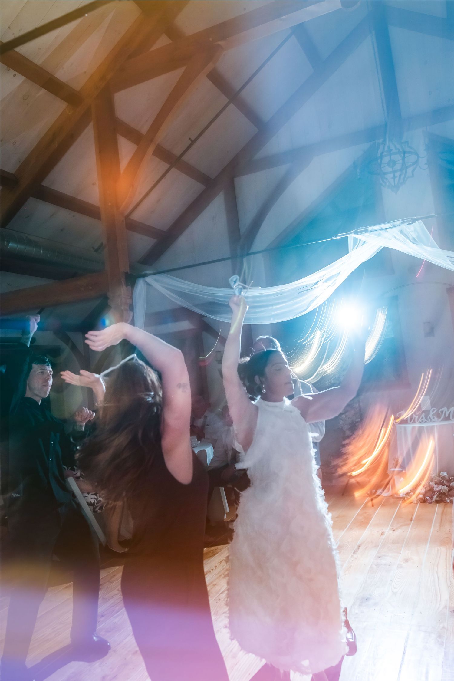 Bride dancing joyfully with guests under draped fabric ceiling at a rustic barn wedding reception.
