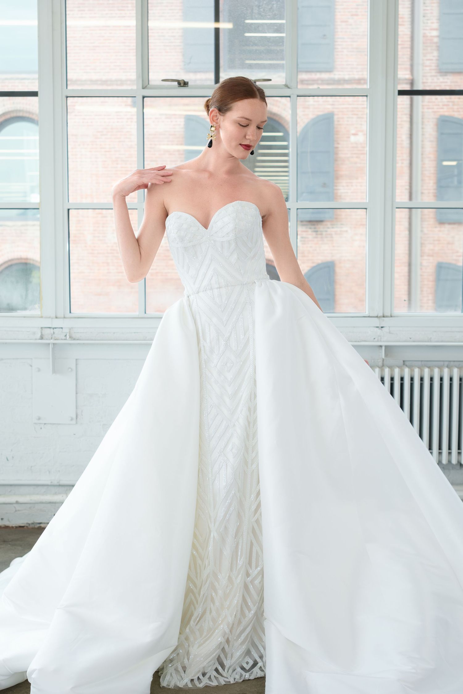 Elegant bride in strapless sweetheart beaded wedding gown with voluminous organza overskirt in bright studio setting.