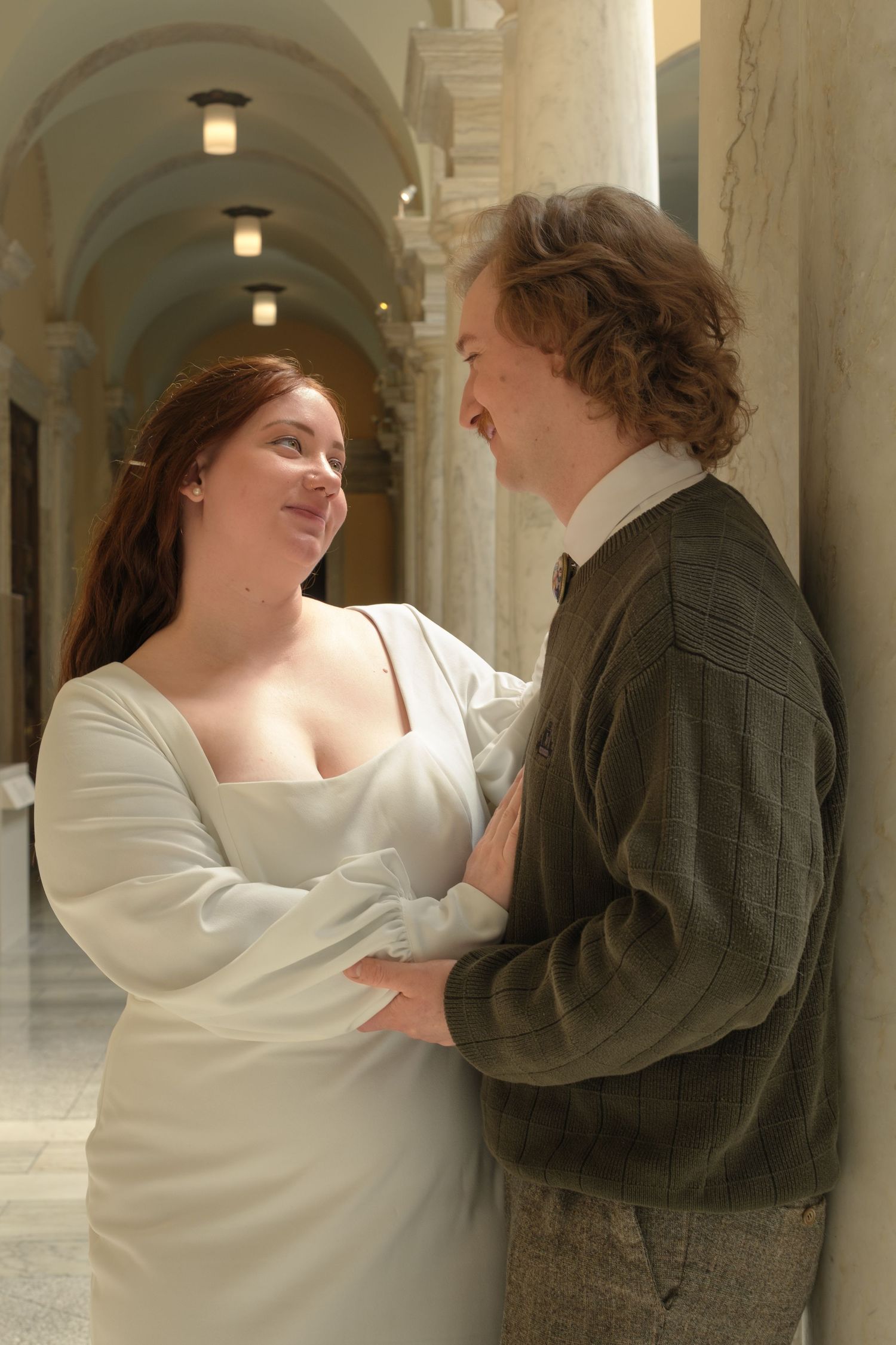 Couple in wedding attire sharing a romantic moment in an elegant columned hallway.