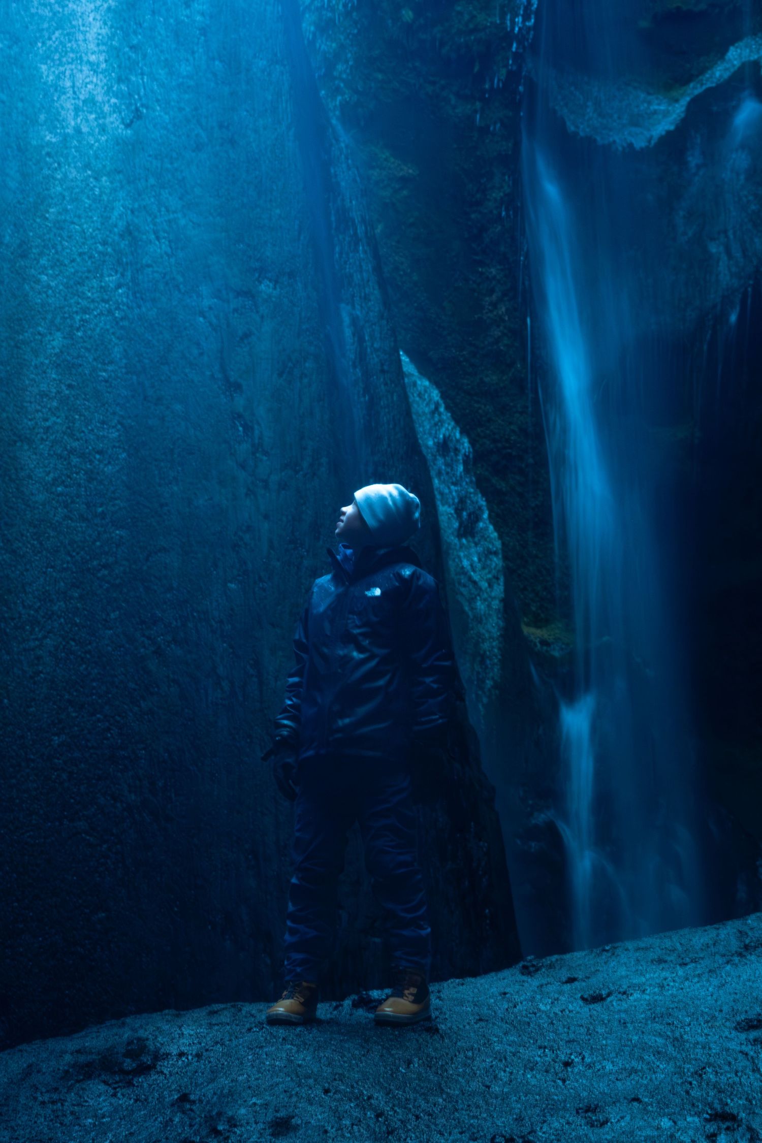A scuba diver explores a dark underwater cave with blue lighting creating an ethereal atmosphere.