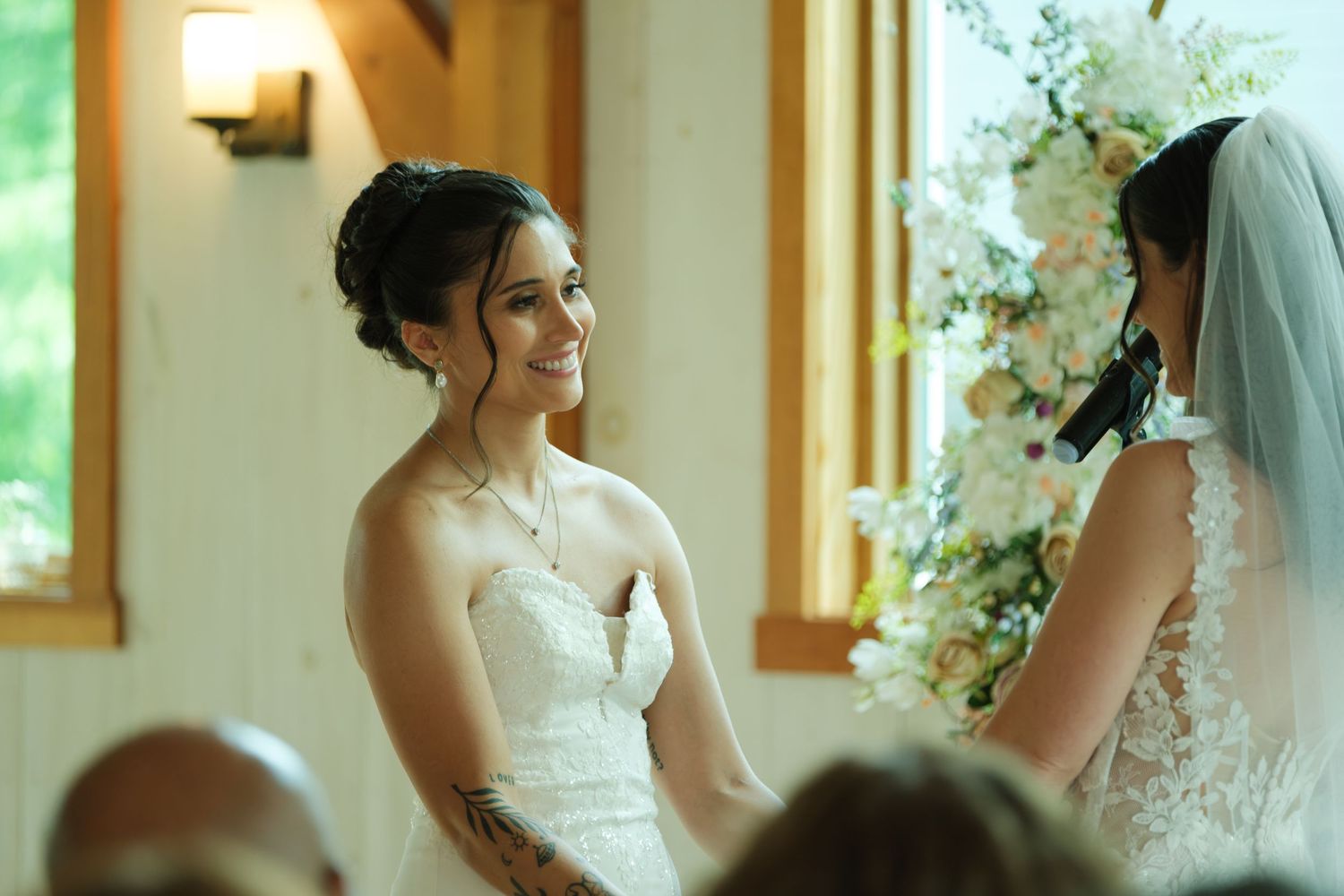 Two brides share a joyful moment at their wedding ceremony, surrounded by floral arrangements in an elegant venue.