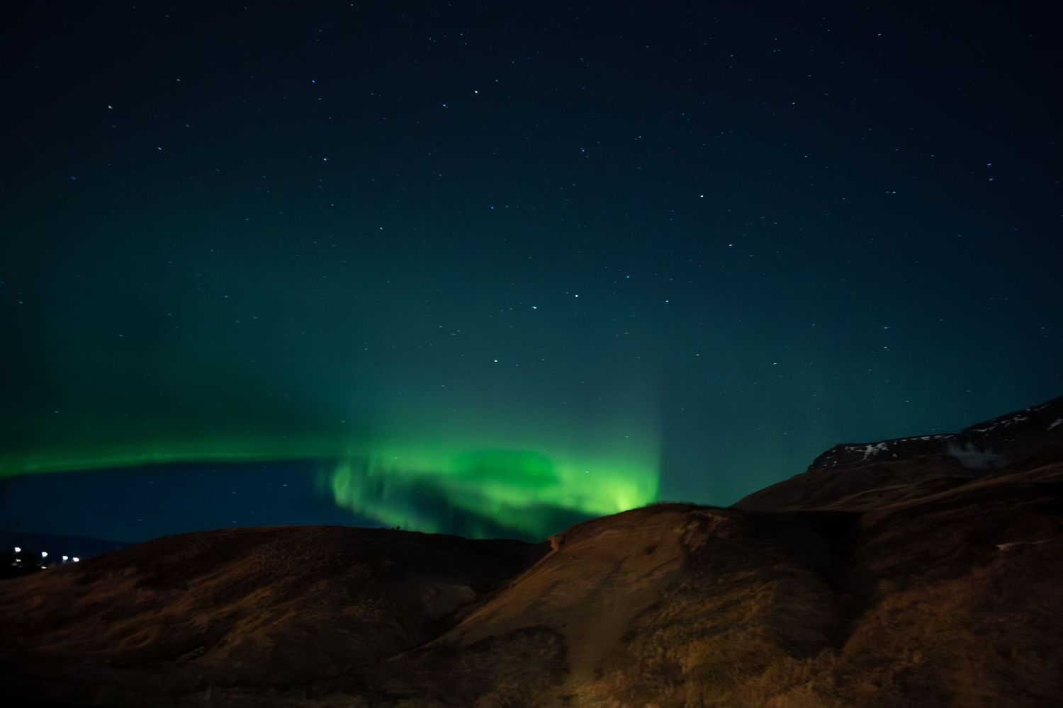 Stunning green aurora borealis dances across the dark night sky above silhouetted mountains in Iceland.