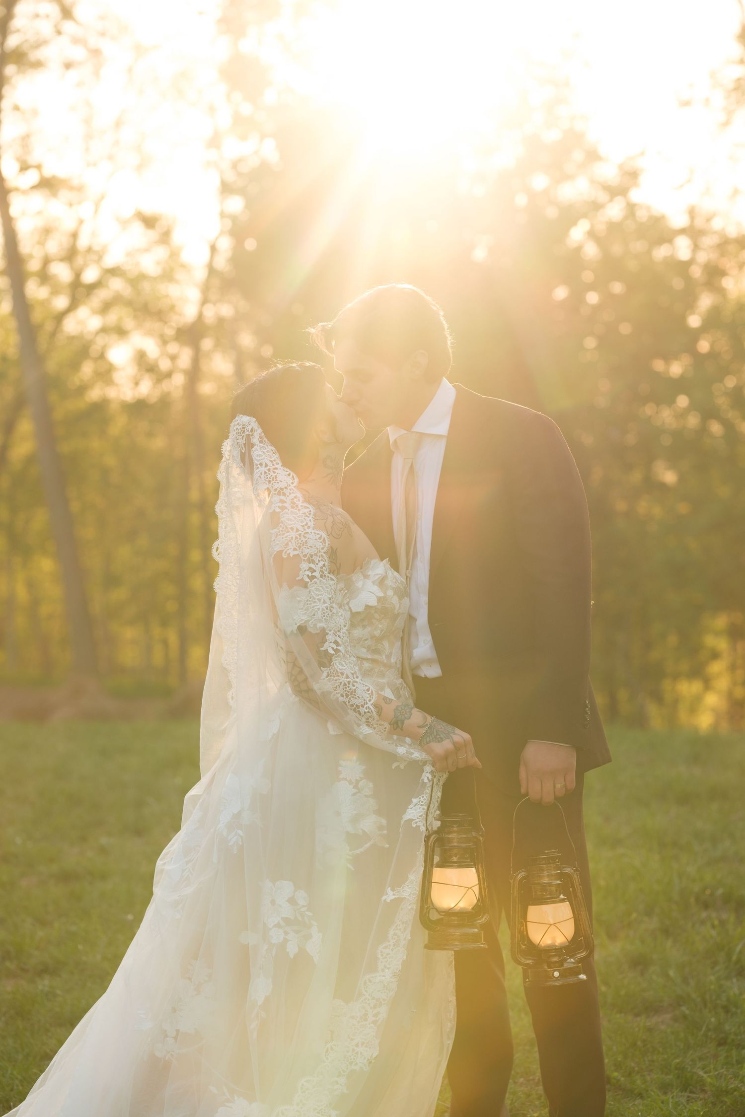 Bride and groom sharing a romantic sunset moment outdoors, groom holding a lantern, bride in lace gown with veil.