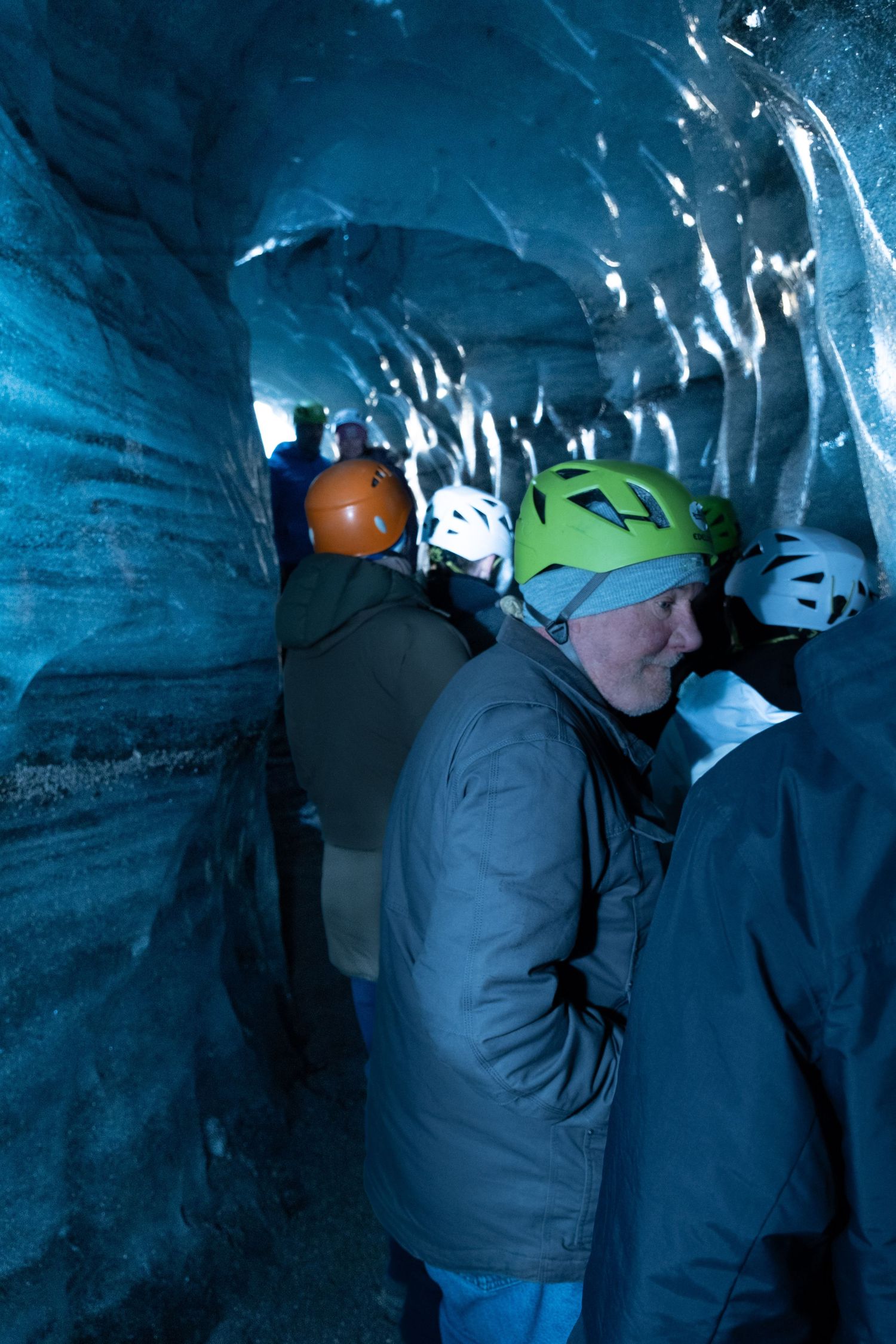 Tourists wearing safety helmets explore a dark blue ice cave during a guided glacier tour in Iceland.