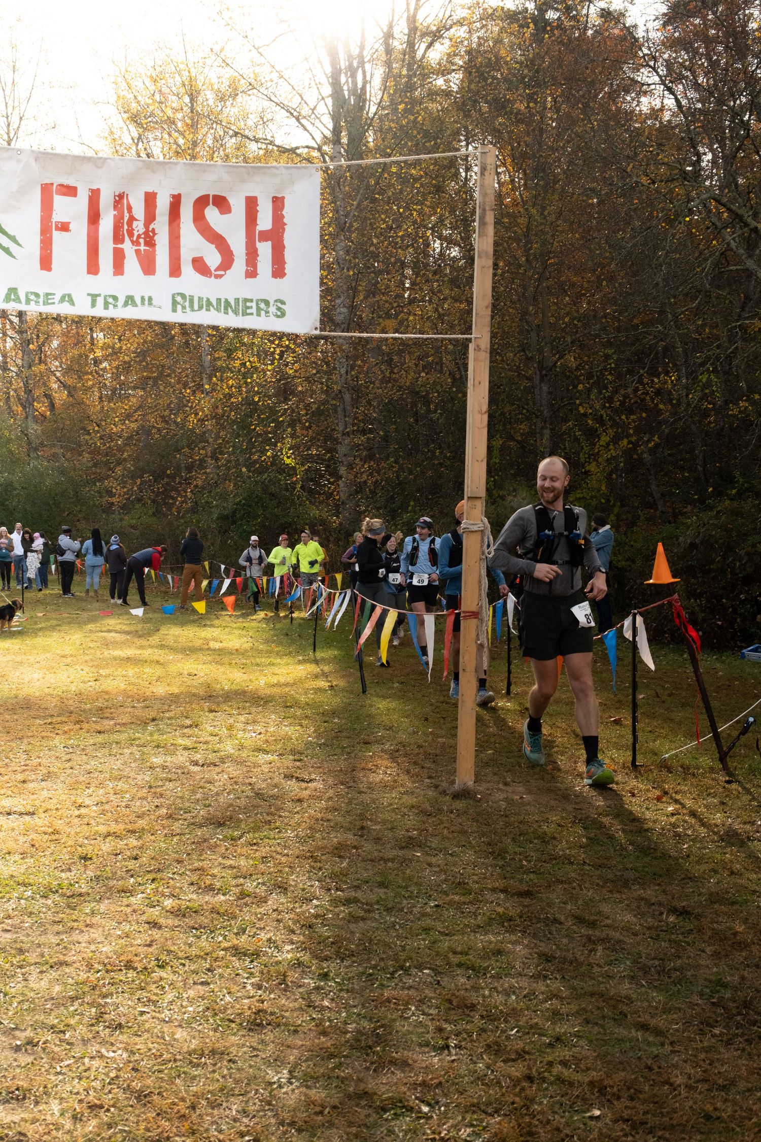 Runners gather at a trail race finish line with autumn trees in the background during an outdoor event.