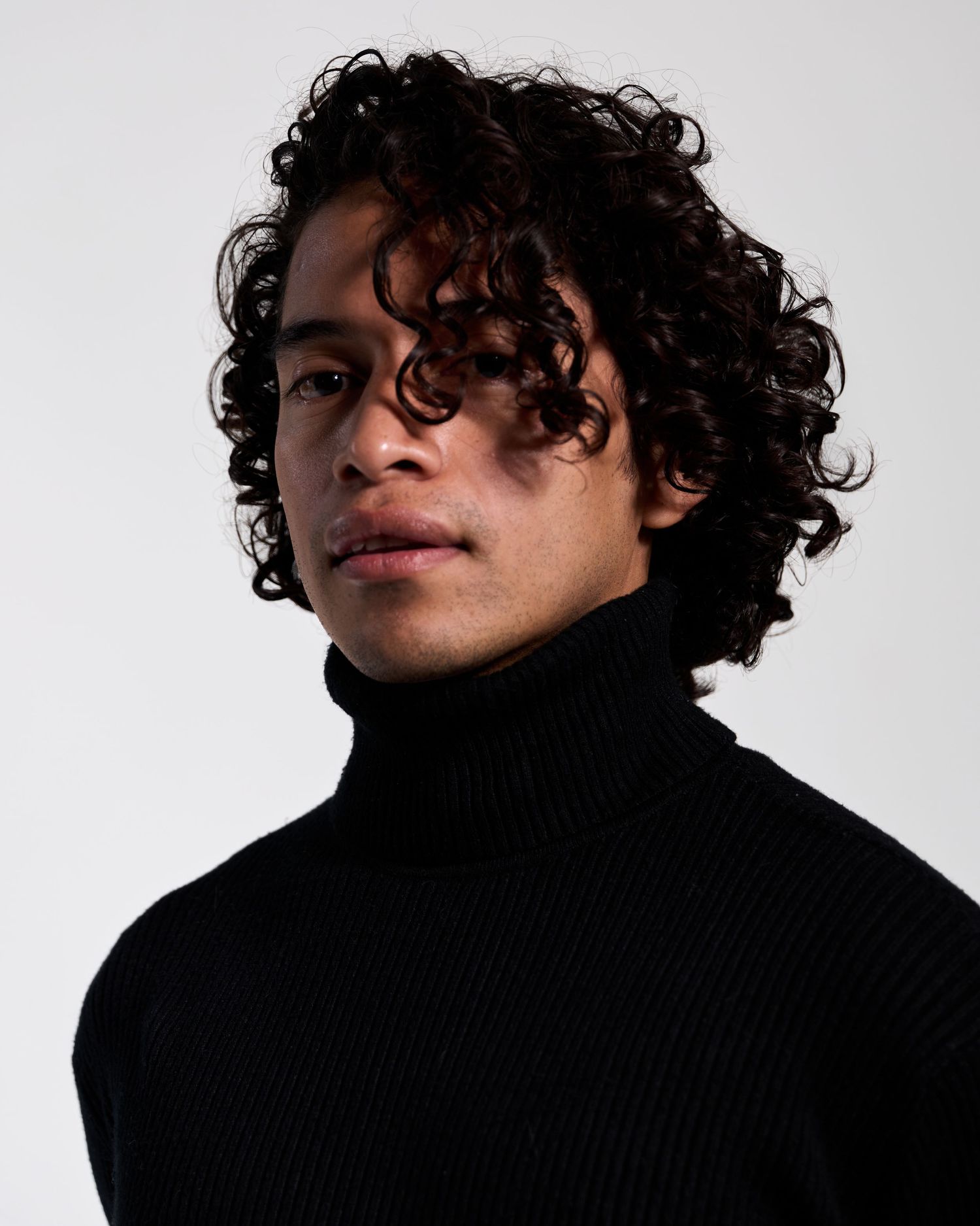 Dramatic black and white portrait series featuring curly hair and turtleneck sweater against white background.
