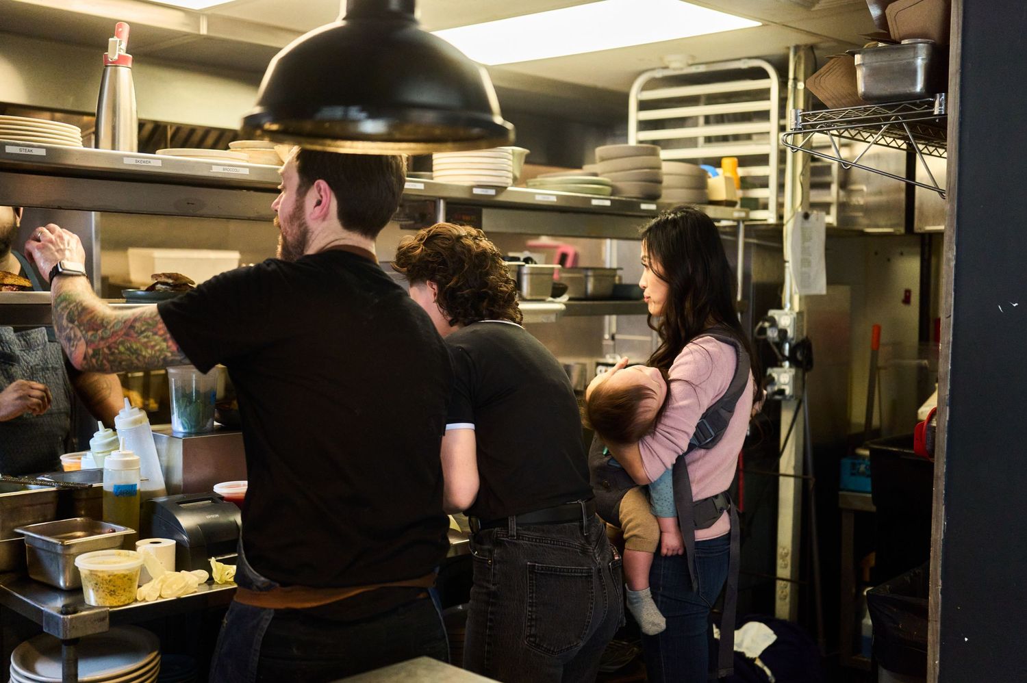 Busy kitchen staff working at food preparation stations in a dimly lit restaurant kitchen.