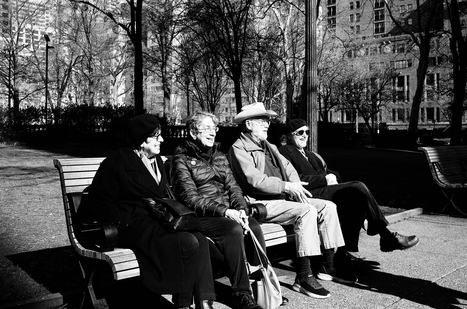 Black and white photograph of people sitting on park benches on a winter day.