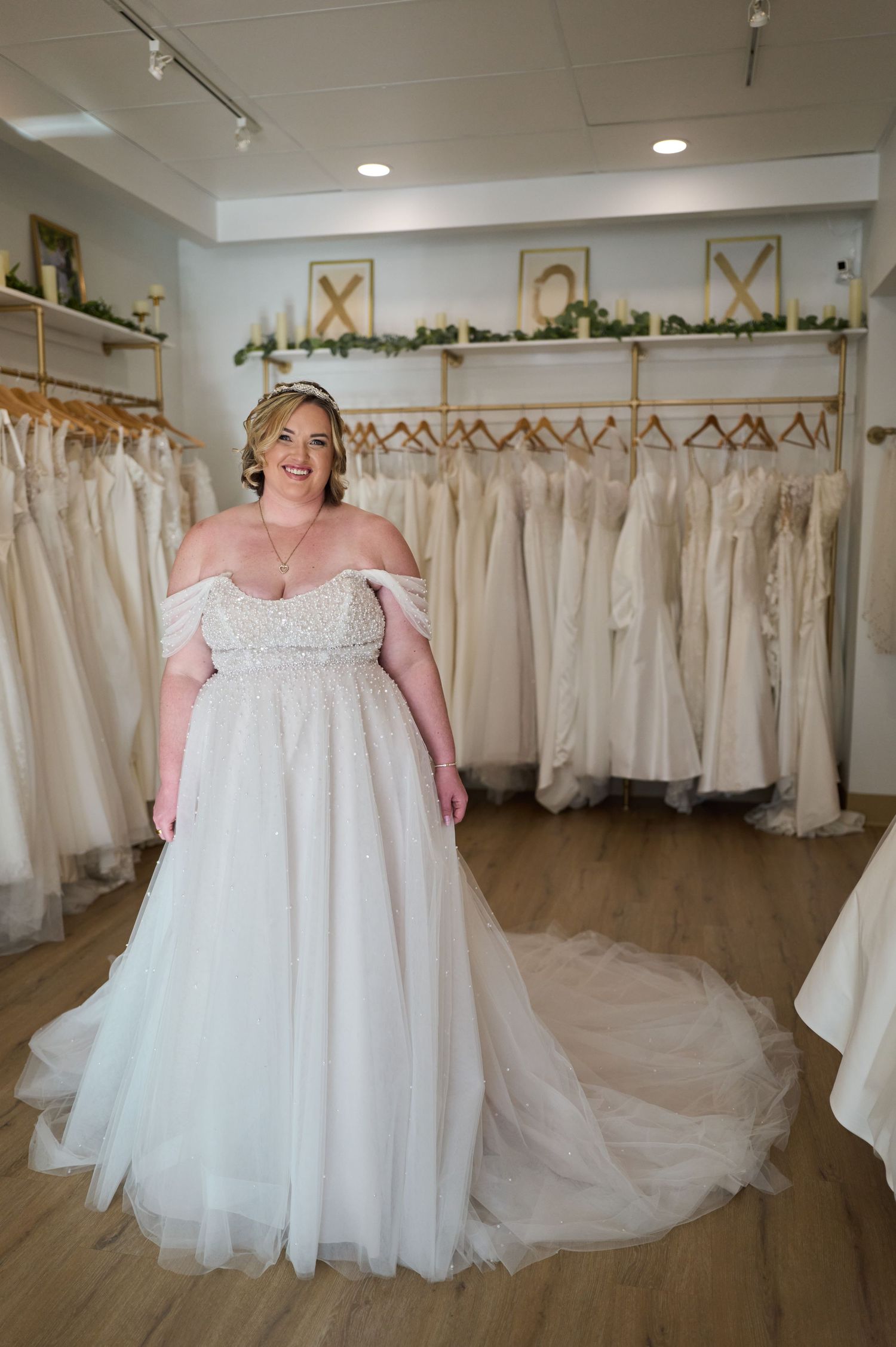 Elegant bridal boutique interior displaying rows of white wedding dresses on hangers with soft lighting and hardwood floors.