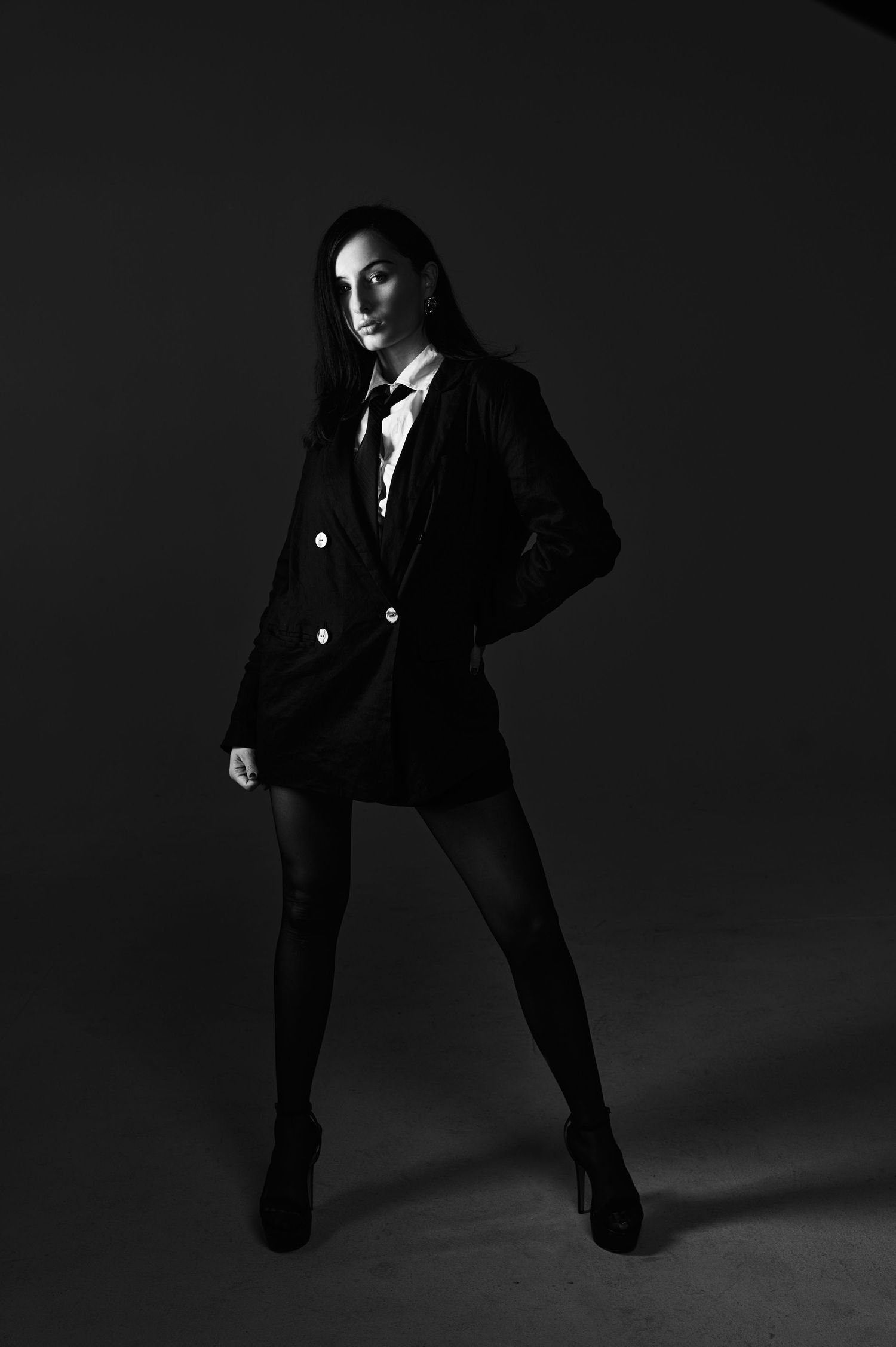 Dramatic black and white fashion photo series showing model in dark blazer striking dynamic poses against dark background.