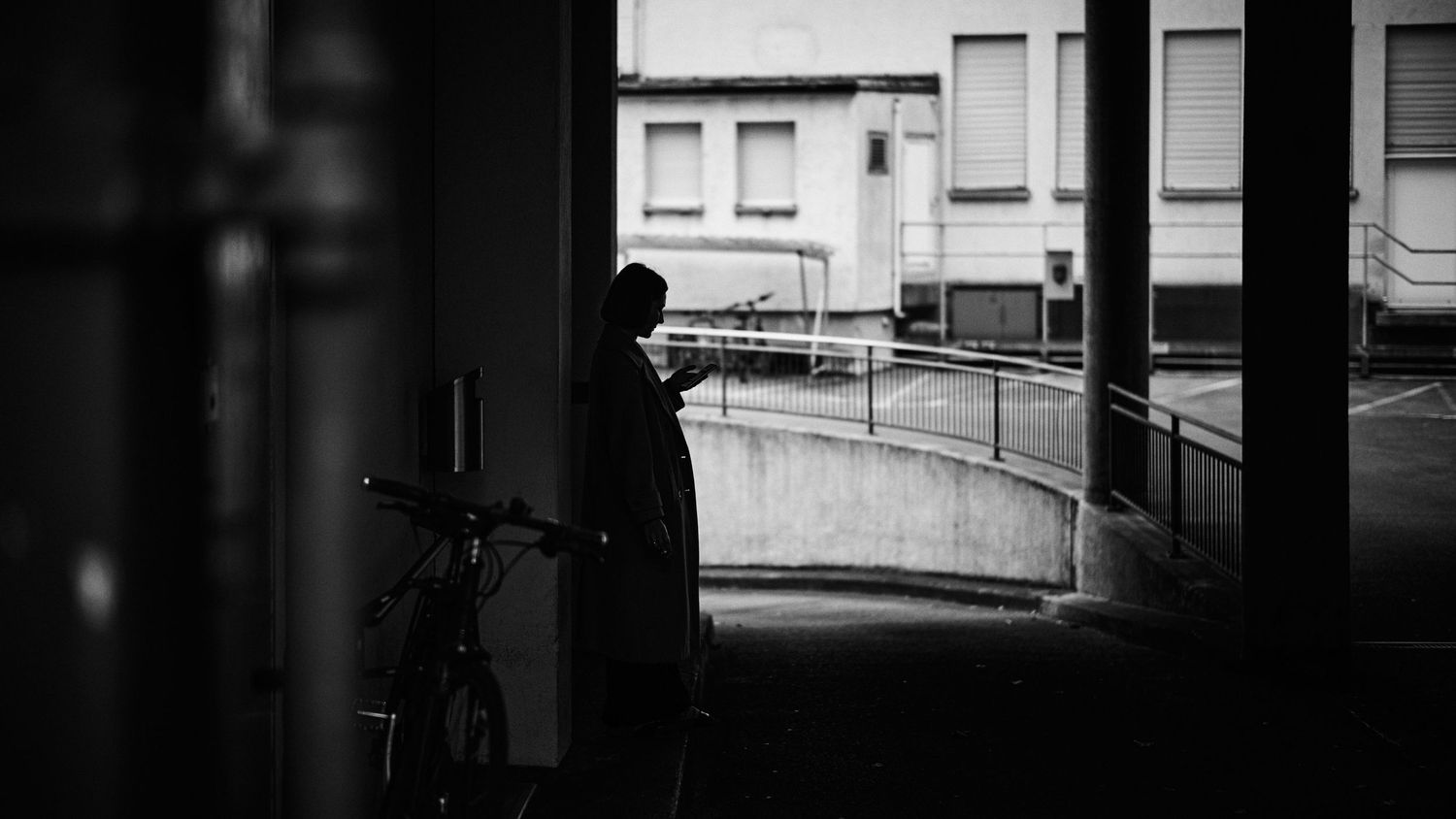 A long empty corridor with black and white tiled flooring leads to a bright window at the end.
