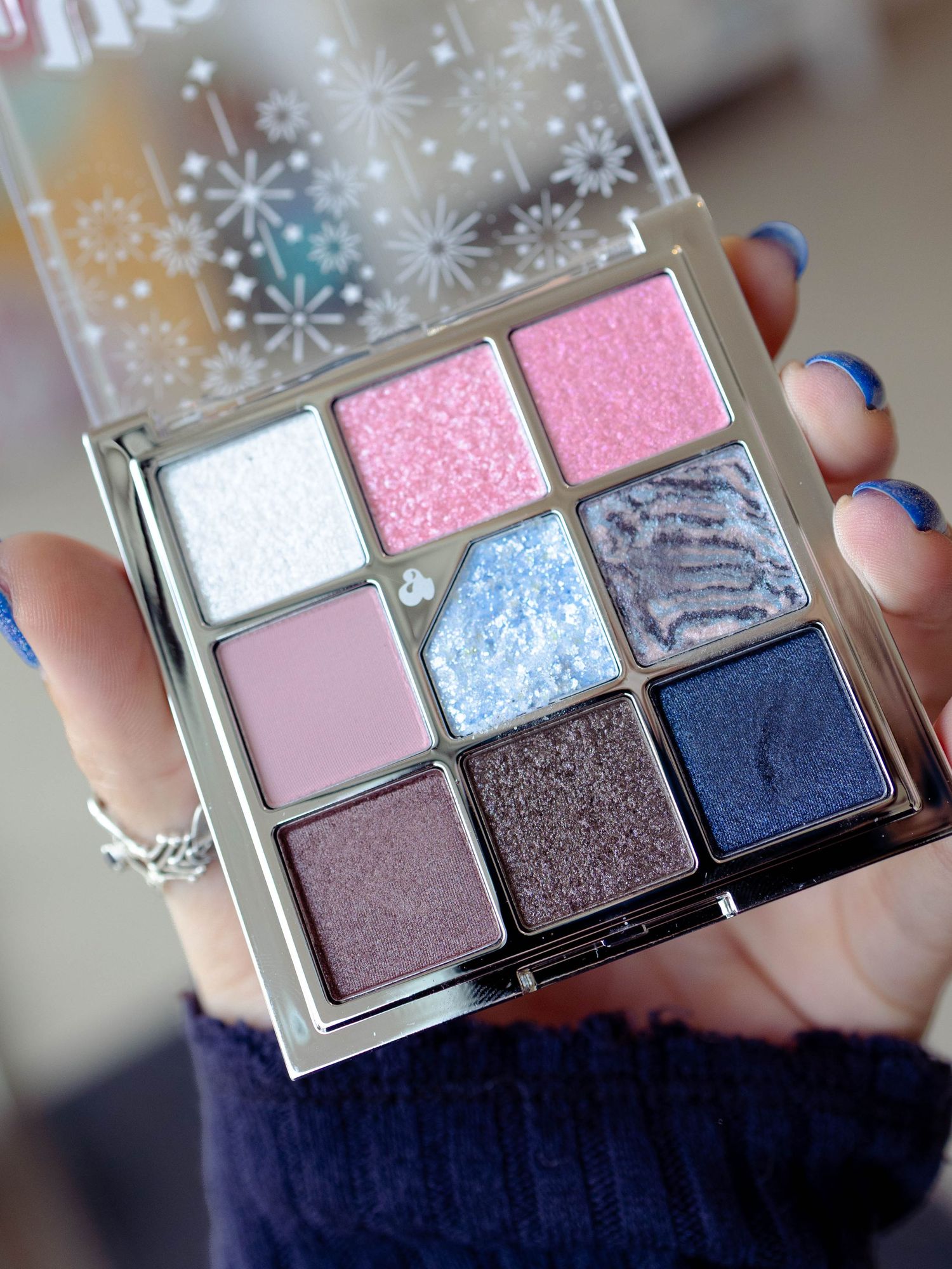 Close-up of woman's hand holdingcolourful eyeshadow palette, showing colours of pinks, blues, purples and shimmer.