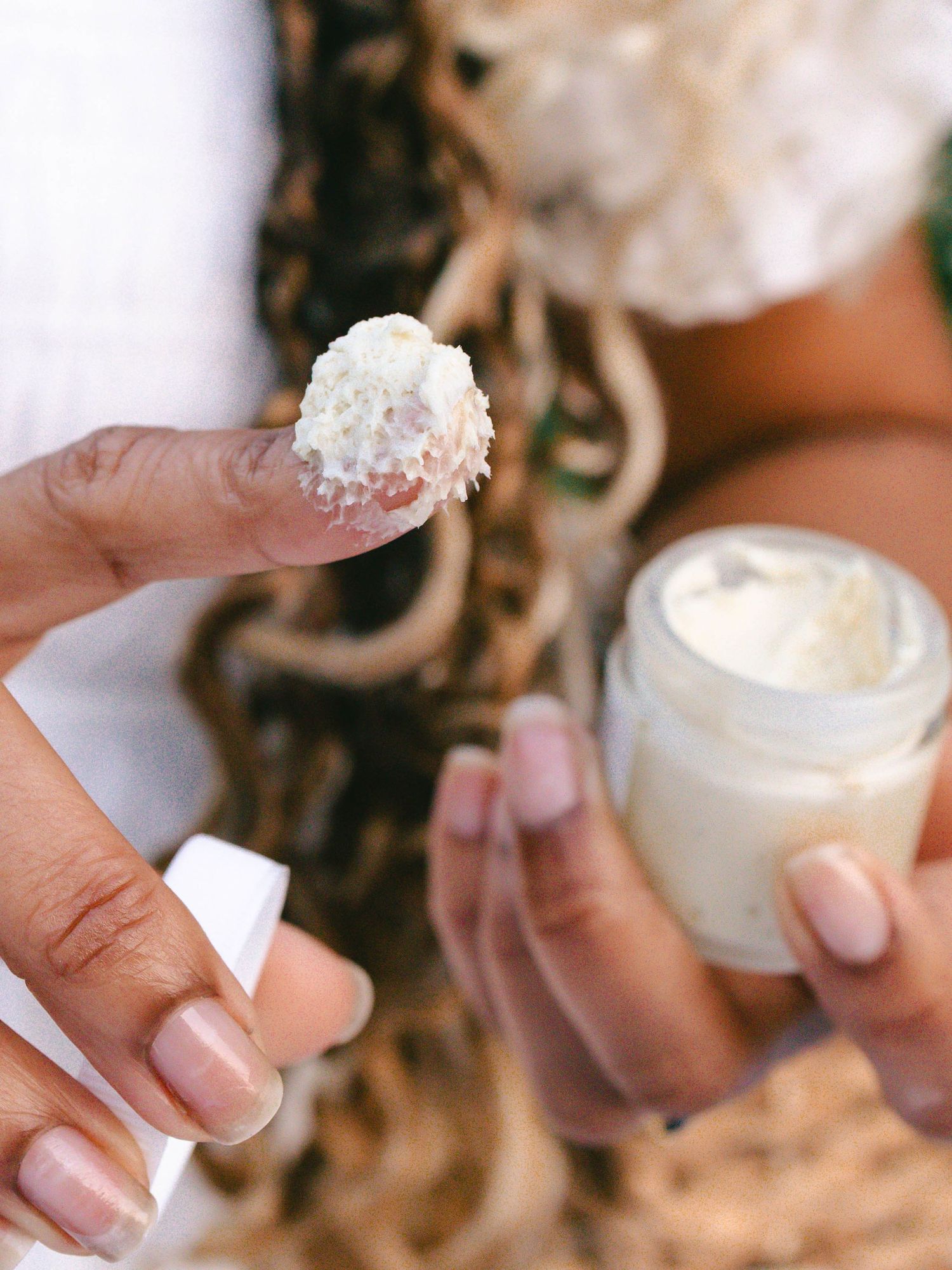 Woman's hands holding skincare product with finger scooping product itself to show whipped creamy texture.