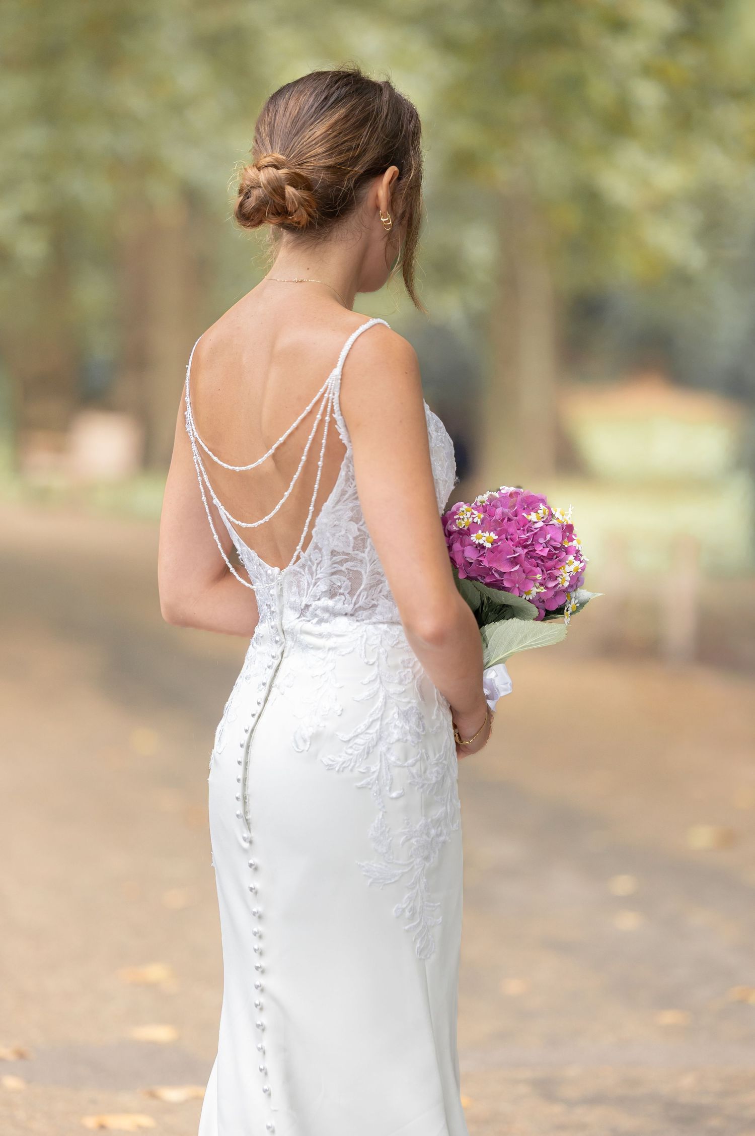 Bride in an elegant backless lace gown holding purple flowers in St James’s Park, London — timeless fine art wedding photography by Alba del