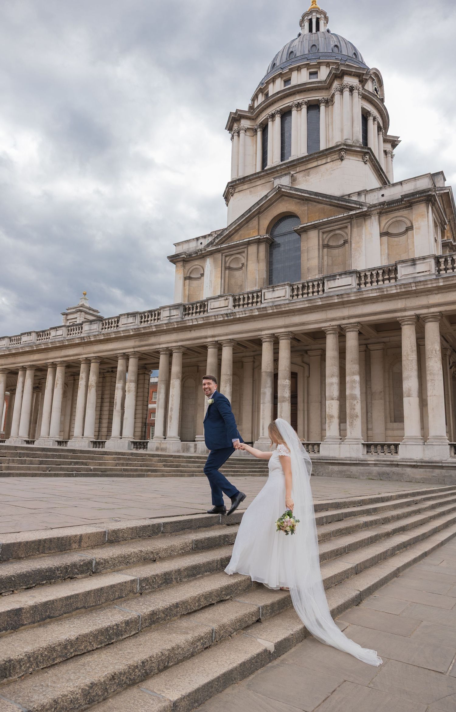 Greenwich Wedding Portrait – Newlyweds holding hands and walking up the steps of the Old Royal Naval College, with its grand columns