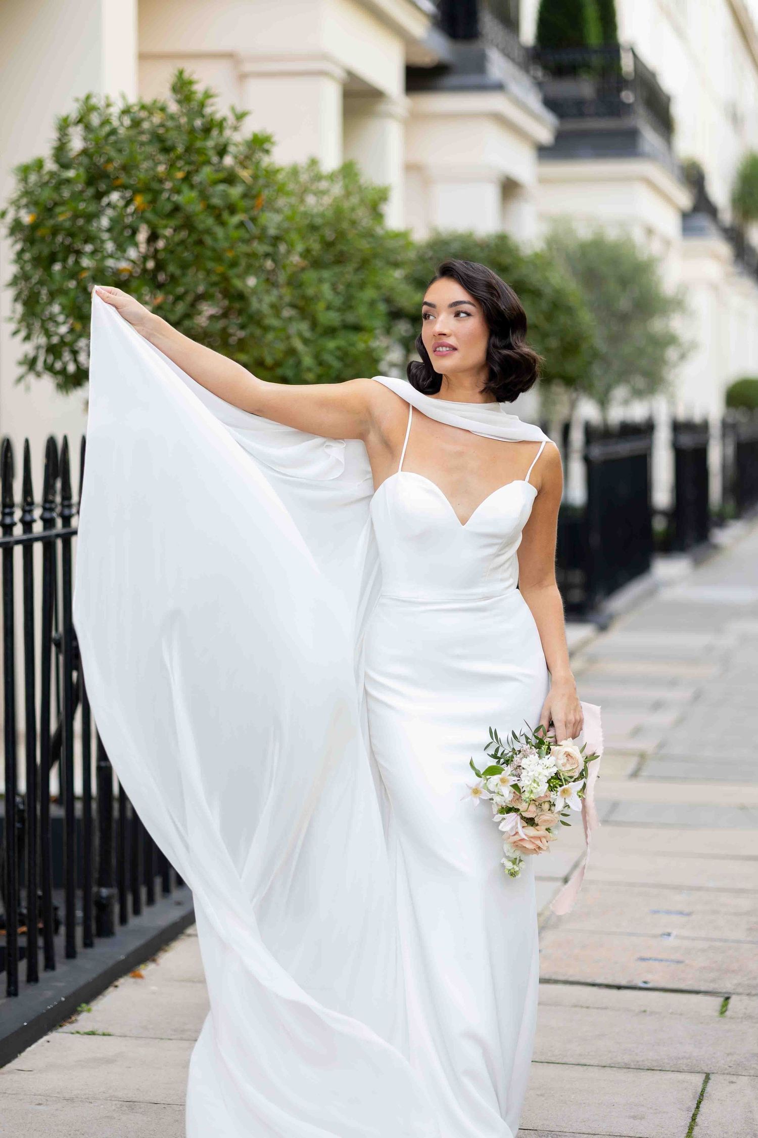 Bride in Belgravia, London – Elegant bride in a sleek white gown holding her bouquet, gracefully lifting her train by Alba del Sol Weddings