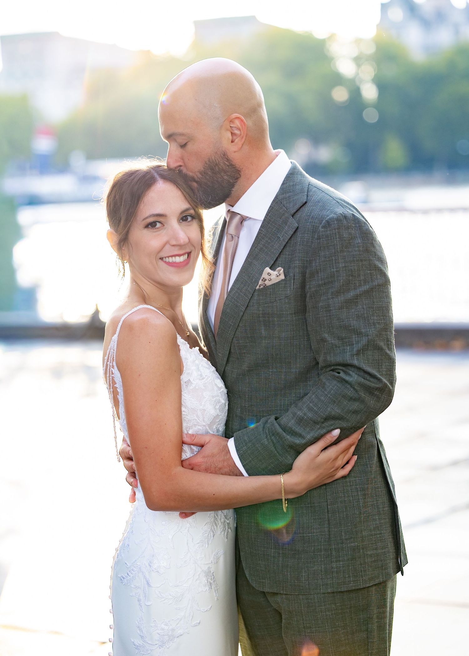 London Riverside Moment – Bride and groom embracing by the riverbank in London, bathed in soft golden sunset light by Alba del Sol