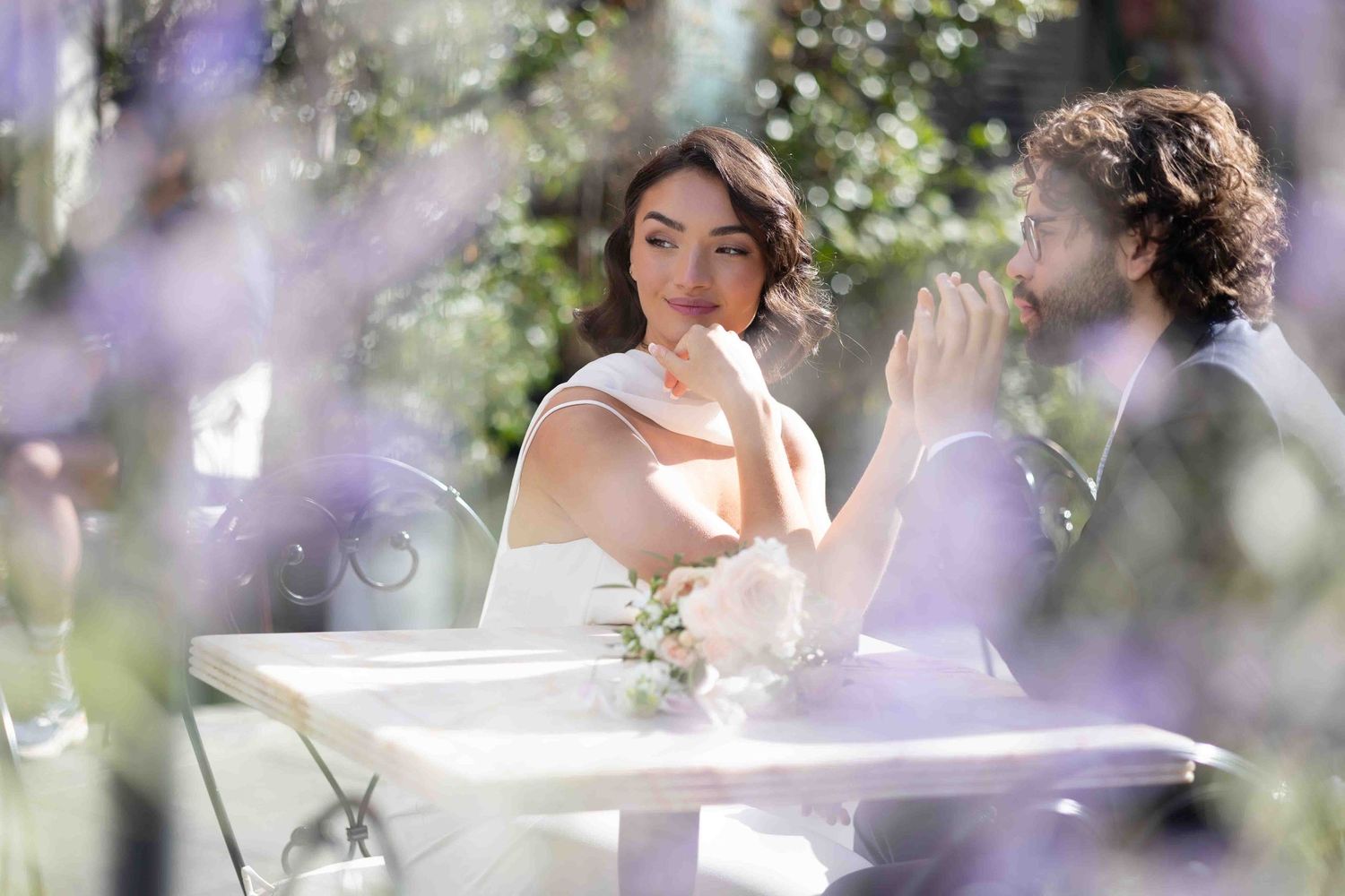 Bride and groom sharing a quiet, romantic moment at a charming outdoor café in Belgravia, London surrounded by soft floral light.