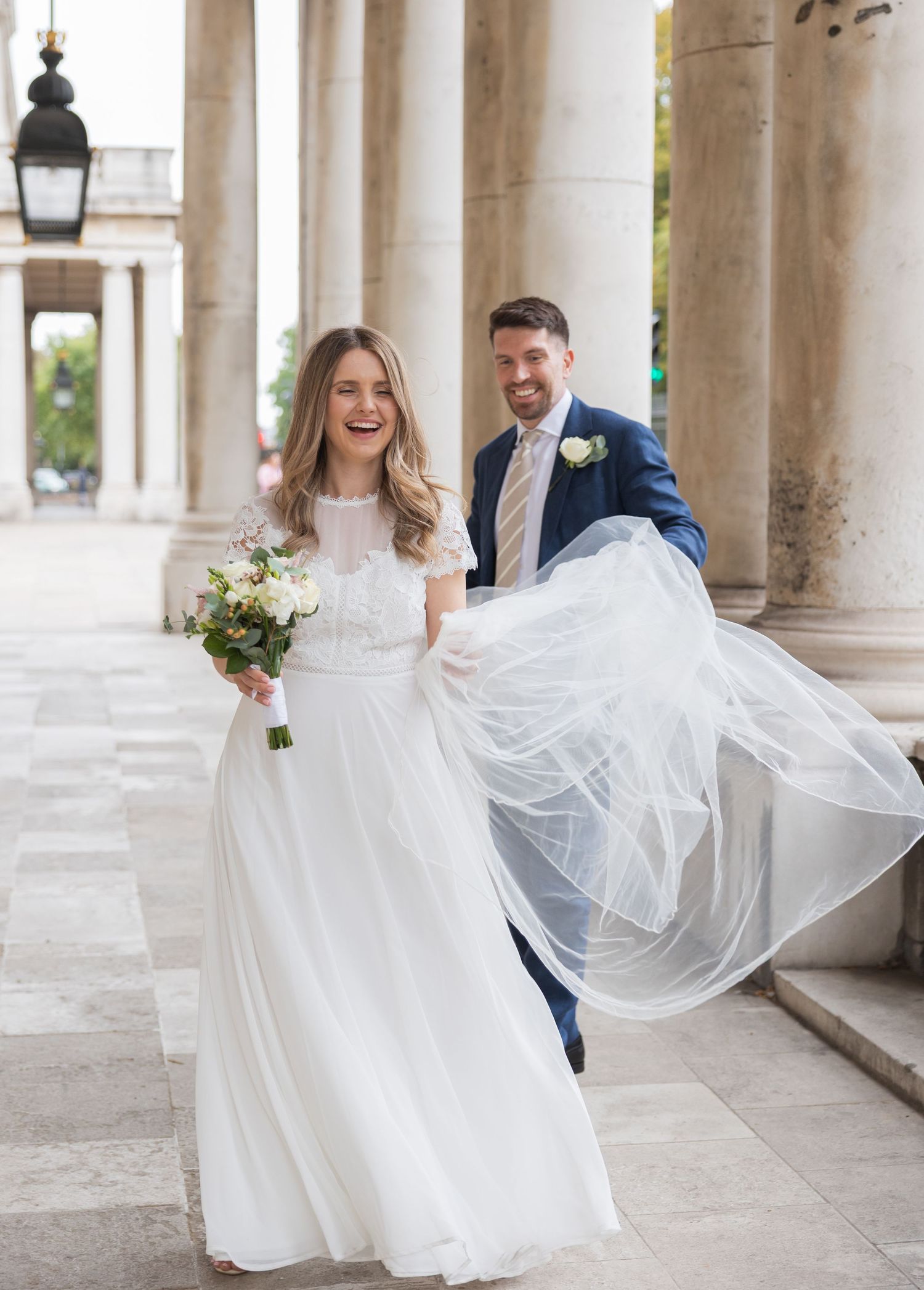 Joyful bride and groom walking under the colonnades of the Old Royal Naval College in London, captured by Alba del Sol, fine art wedding