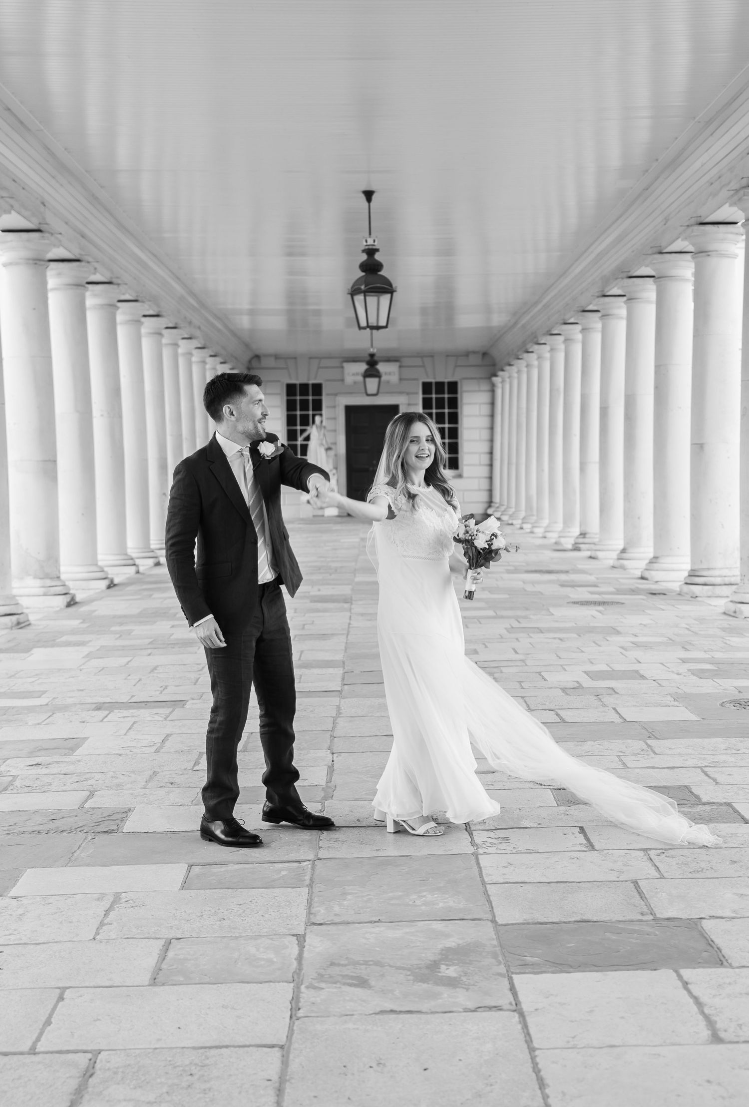 Black-and-white photo of a couple dancing joyfully on their wedding day, beneath the historic Queen house in Greenwich, London