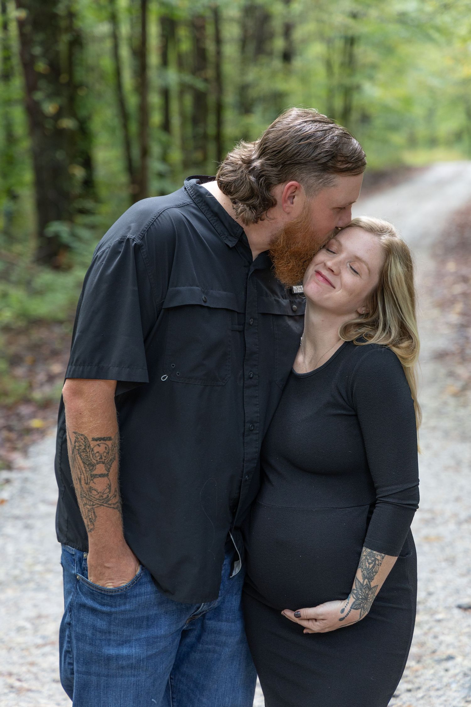 Man and woman kissing while holding each other down a forest road