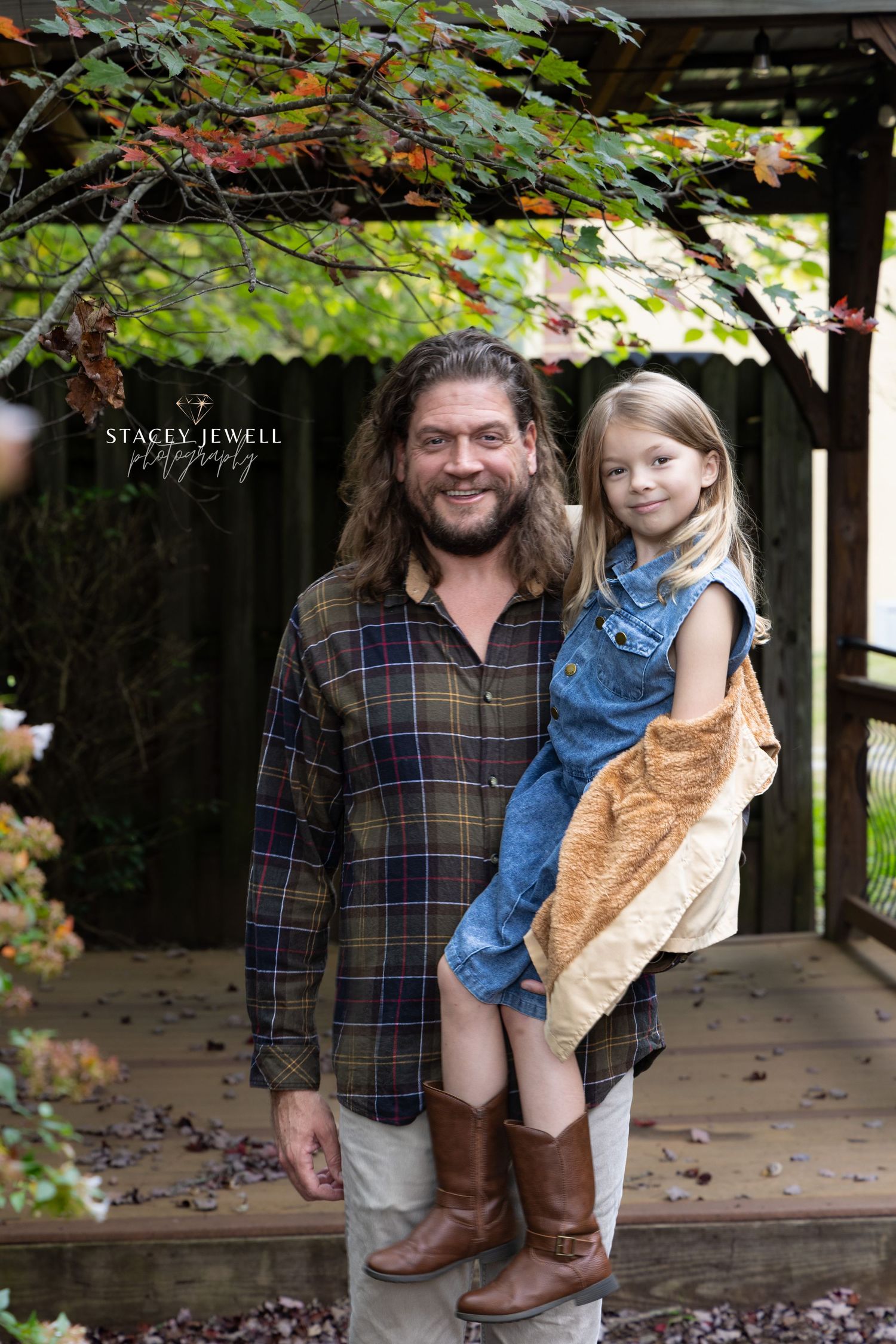 Dad holding daughter under an autumn tree and pavillion