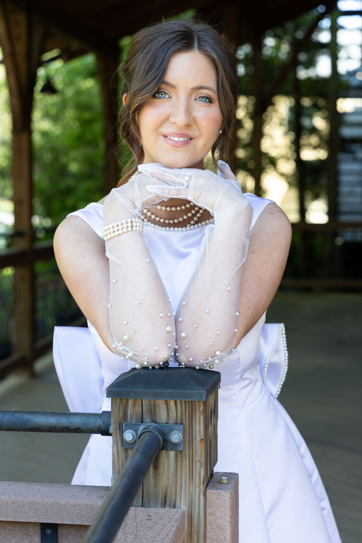 Bridal portraiture of beautiful bride in classic white dress, gloves and pearls under a pavillion