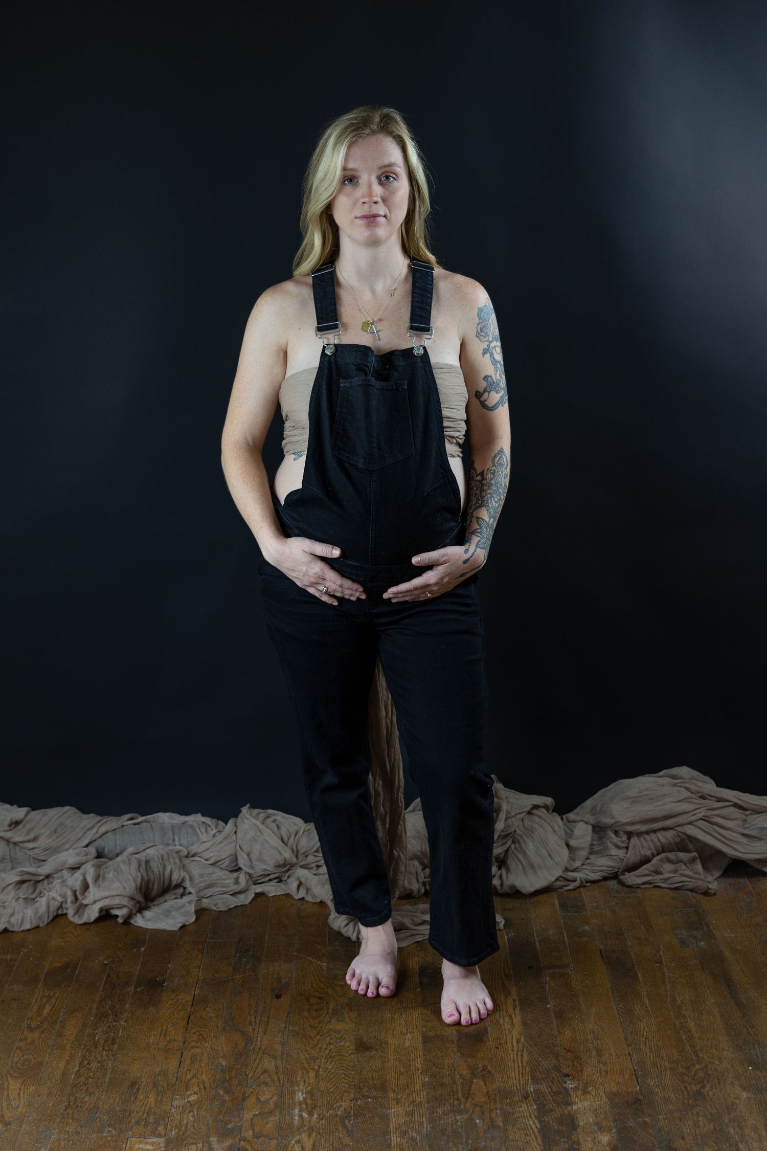 Pregnant mother in black overalls holding her belly