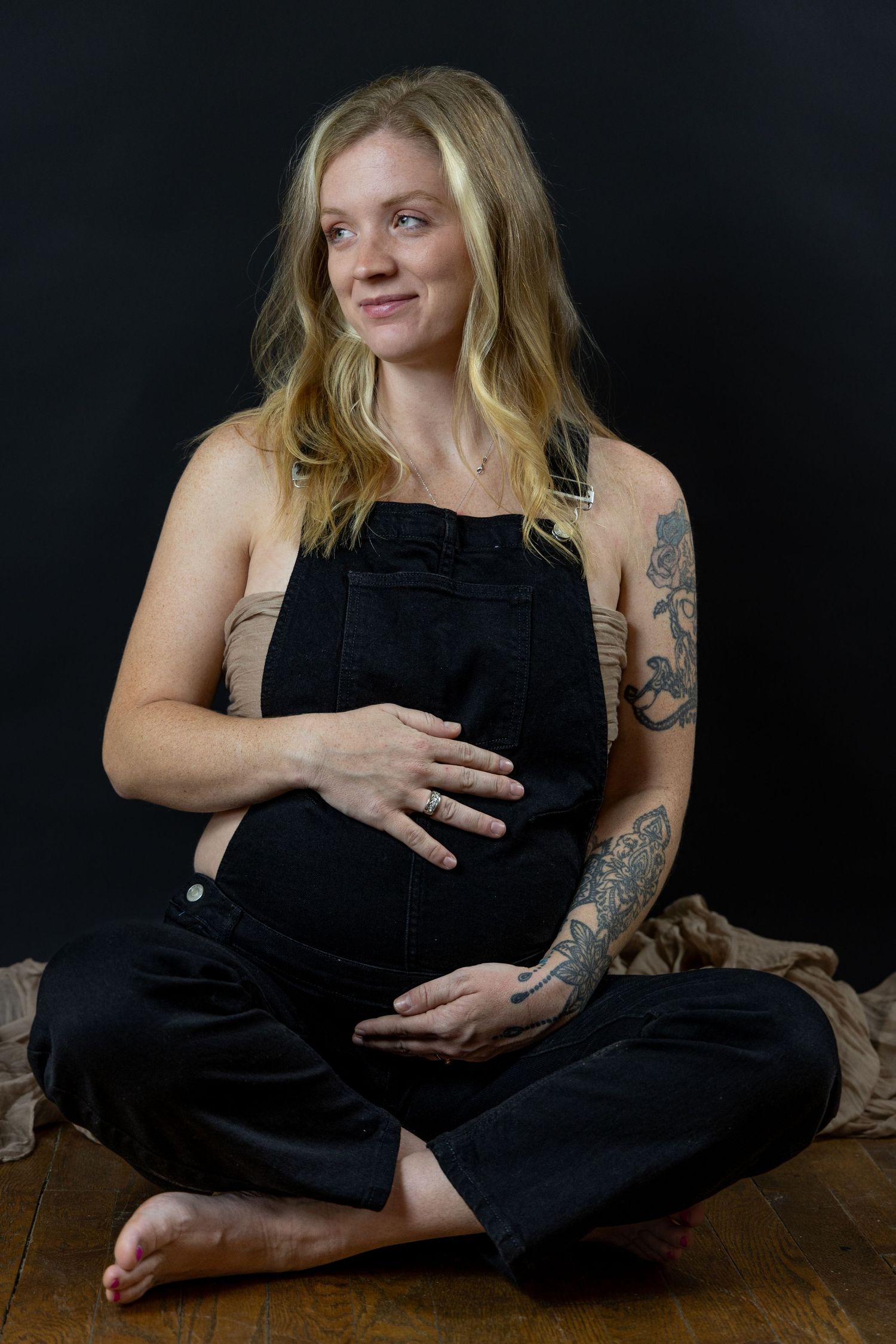 Portraiture of a pregnant mother in black overalls holding her belly