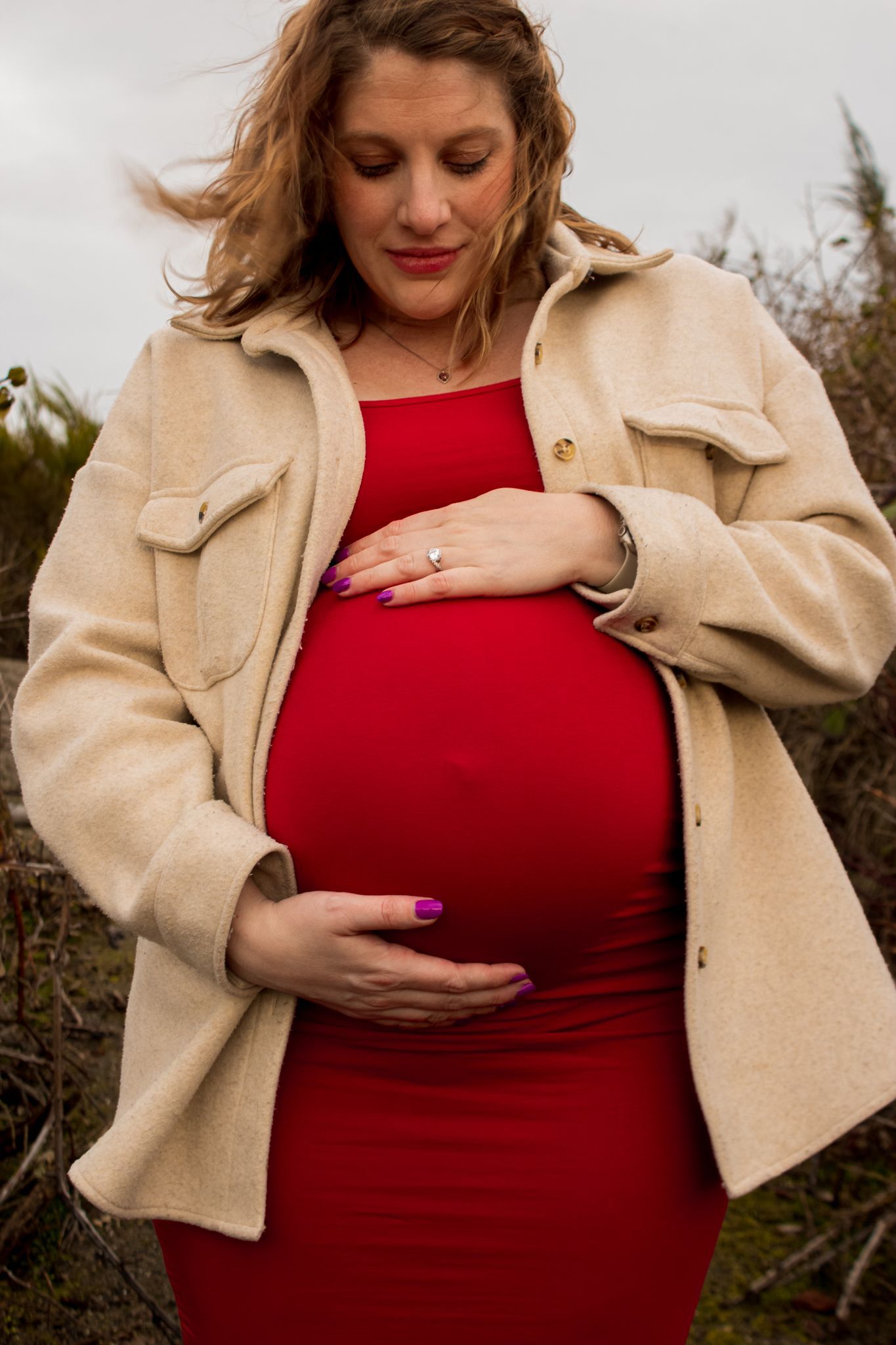 Maternity photos on the beach. Candid maternity photo. Moody. tall grass in the background. dark skies. Windy day