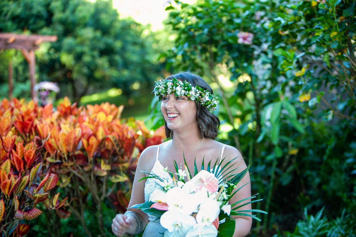 Wedding attendant wearing floral crown and holding tropical bouquet in lush garden setting in Kauai.