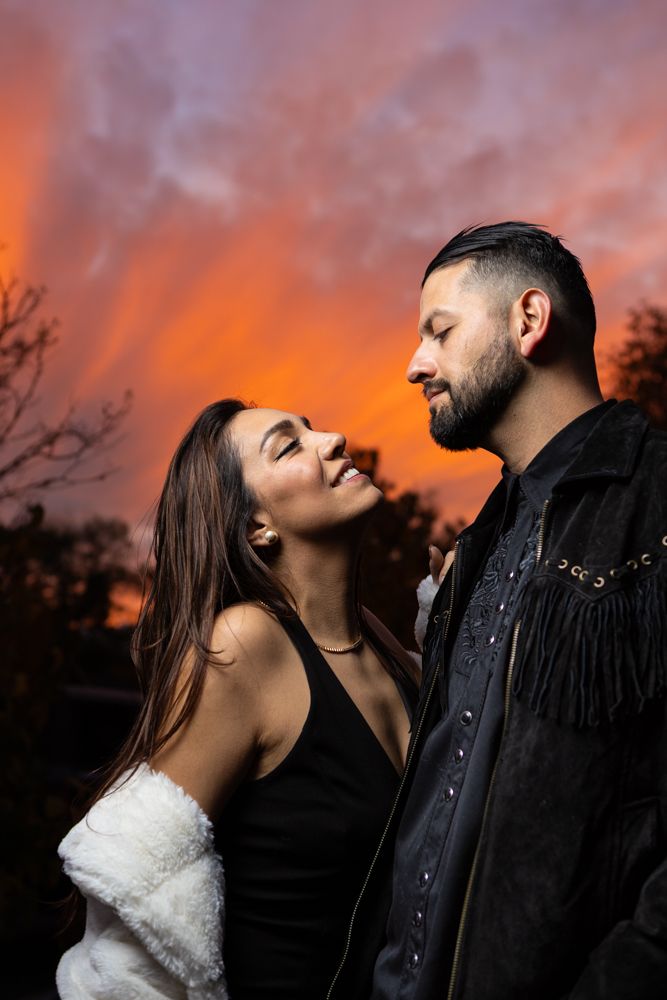 Romantic couple posing against dramatic orange sunset sky.