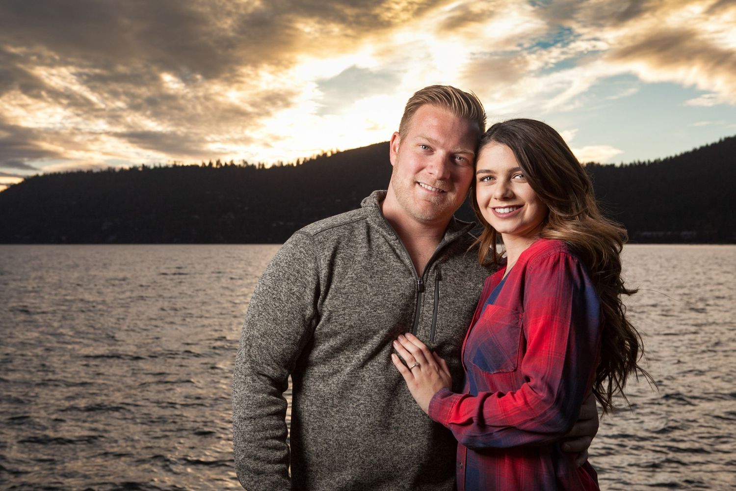 Romantic sunset engagement photo session by a lake with dramatic golden clouds and mountains in Lake Tahoe.