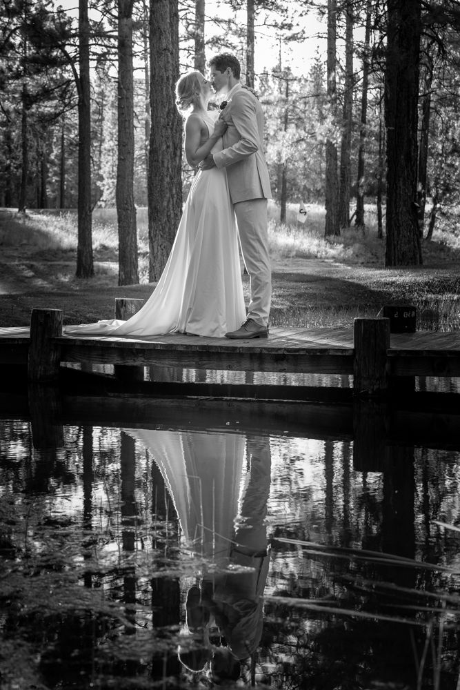 Black and white reflection of a couple on a wooden dock over still water.