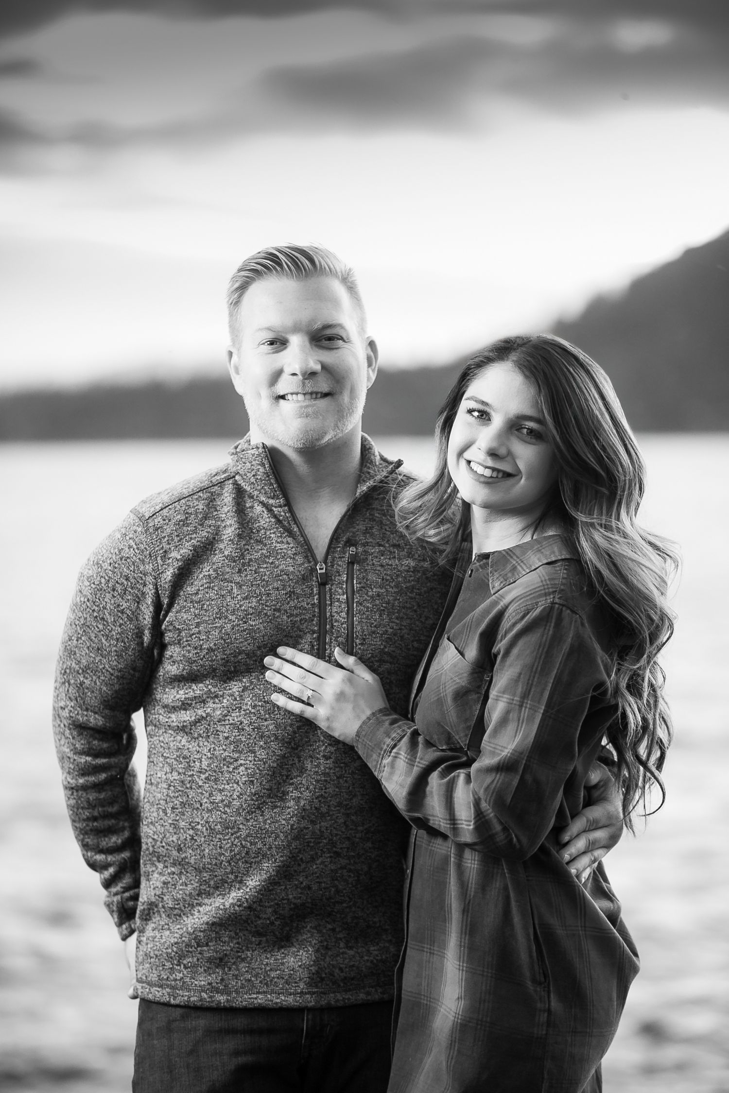 Black and white portrait series of couple in casual attire against scenic lake background.