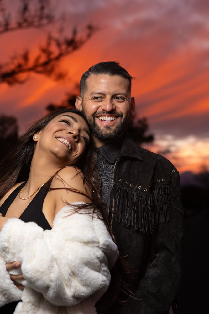 Joyful couple laughing together during sunset photoshoot.