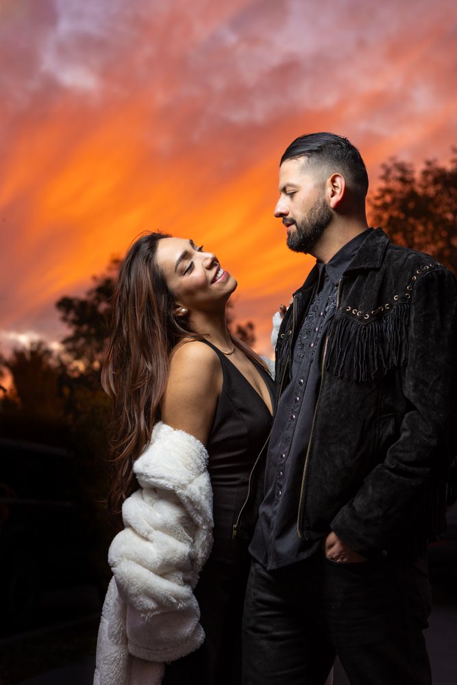 Couple in contrasting black and white outfits against fiery sunset.