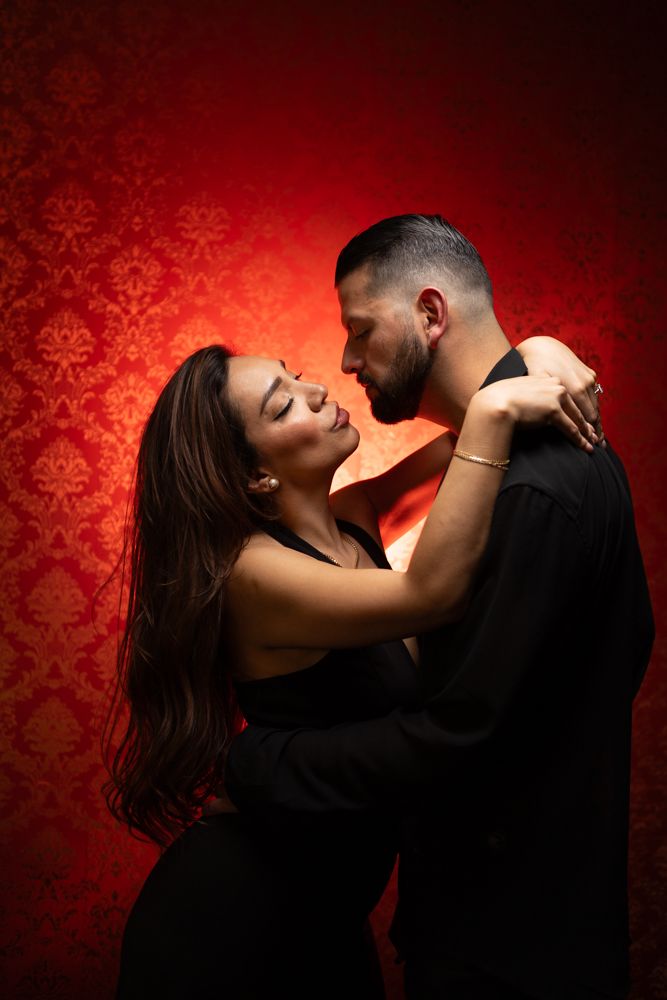Romantic couple embracing against a red damask wallpaper background.