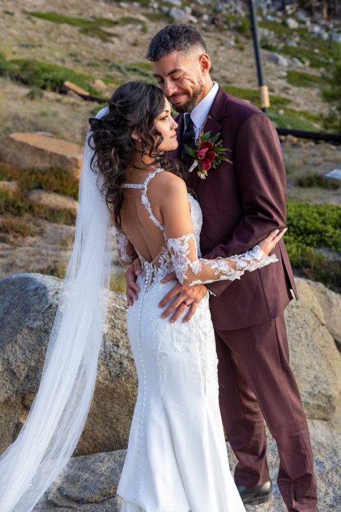 Couple in burgundy suit and lace wedding dress posing on rocky mountain terrain in Heavenly Mountain resort Lake Tahoe.