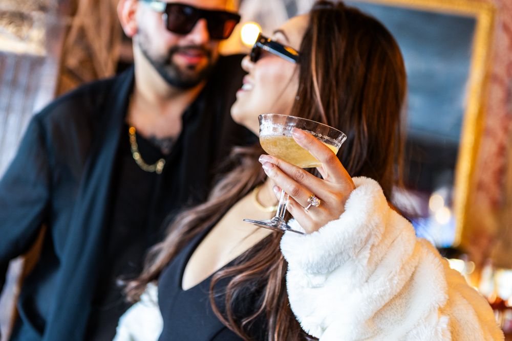 A stylish couple wearing sunglasses poses together in casual attire.