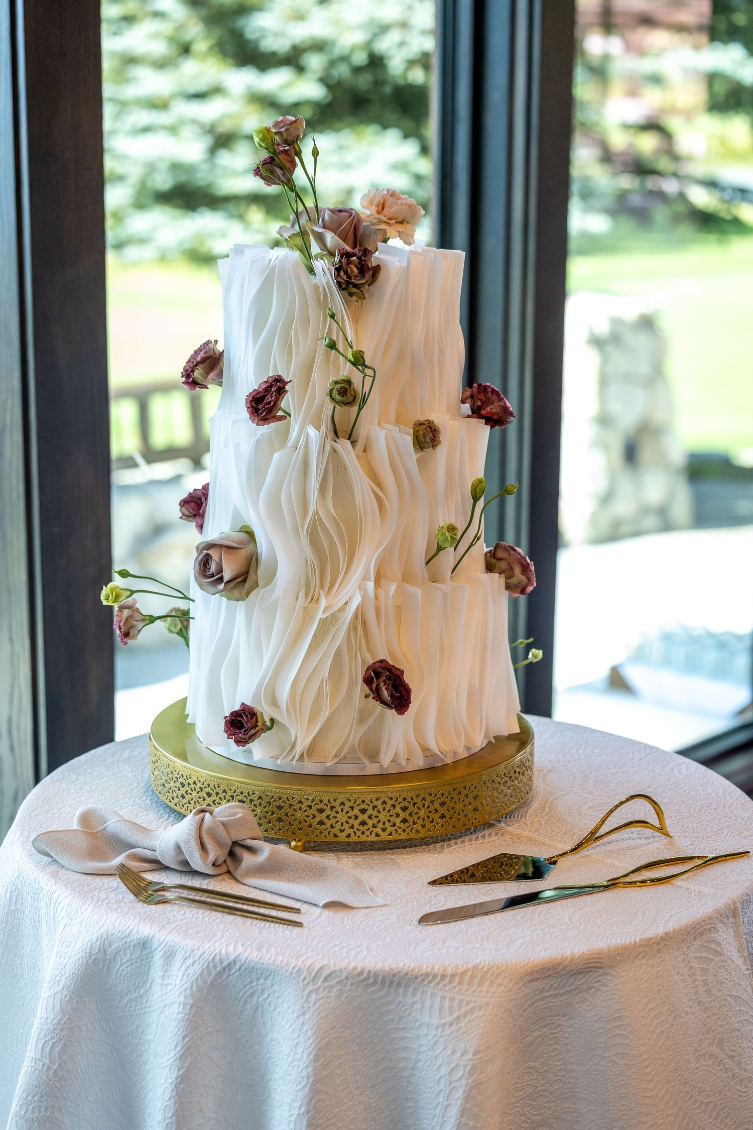 White wedding cake decorated with delicate burgundy sugar flowers on a textured tablecloth.