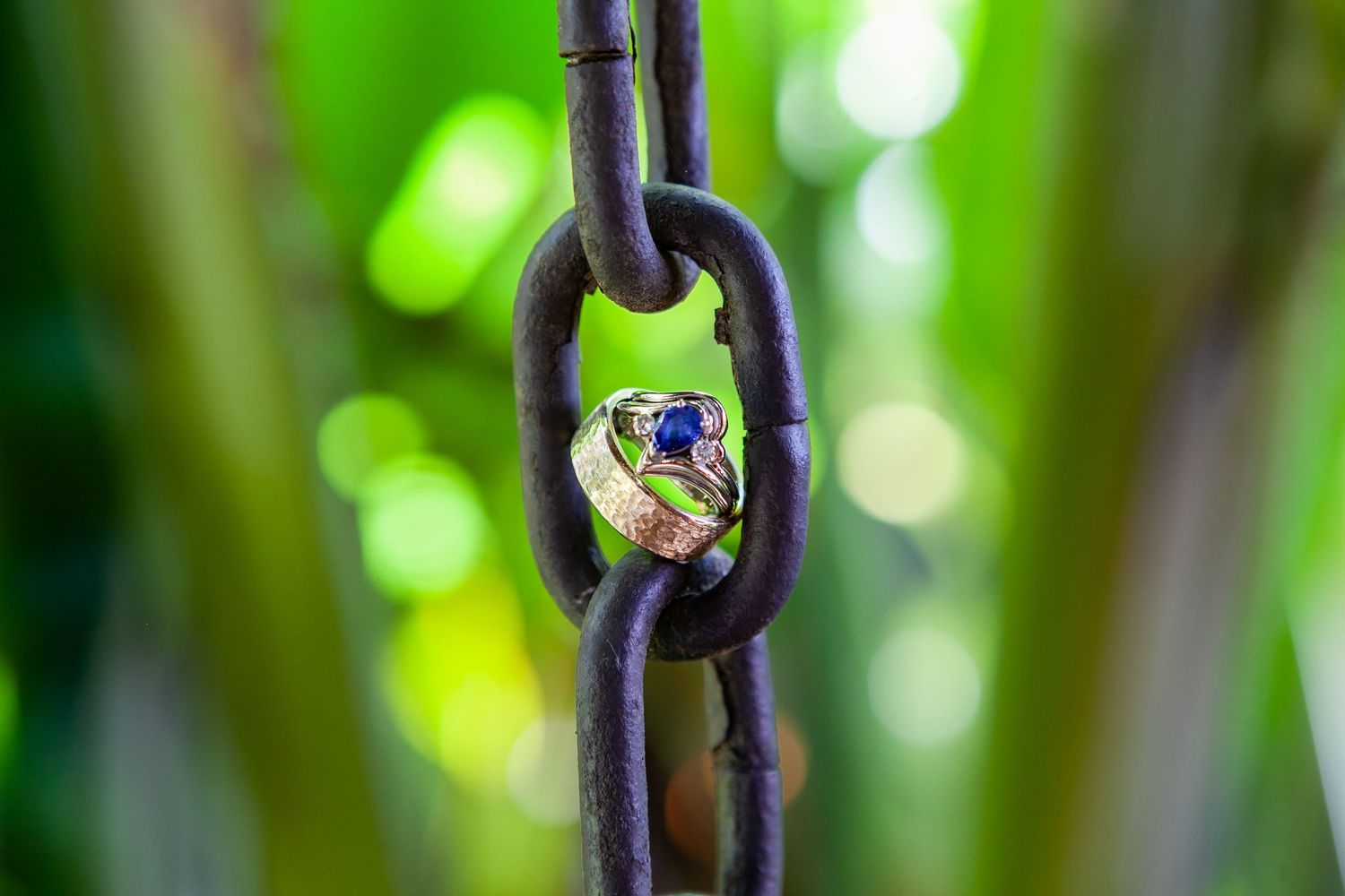 Wedding ring photographed on a rustic metal chain with green bokeh background.