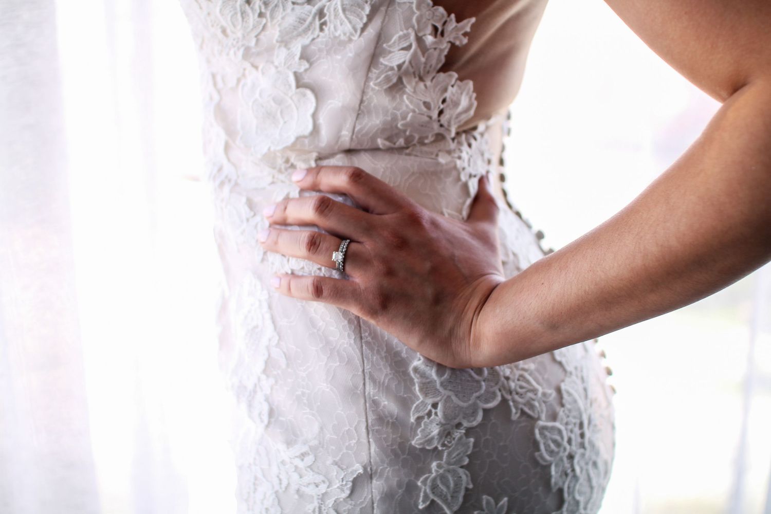 A bride in a white lace wedding dress with delicate floral details and sheer sleeves.